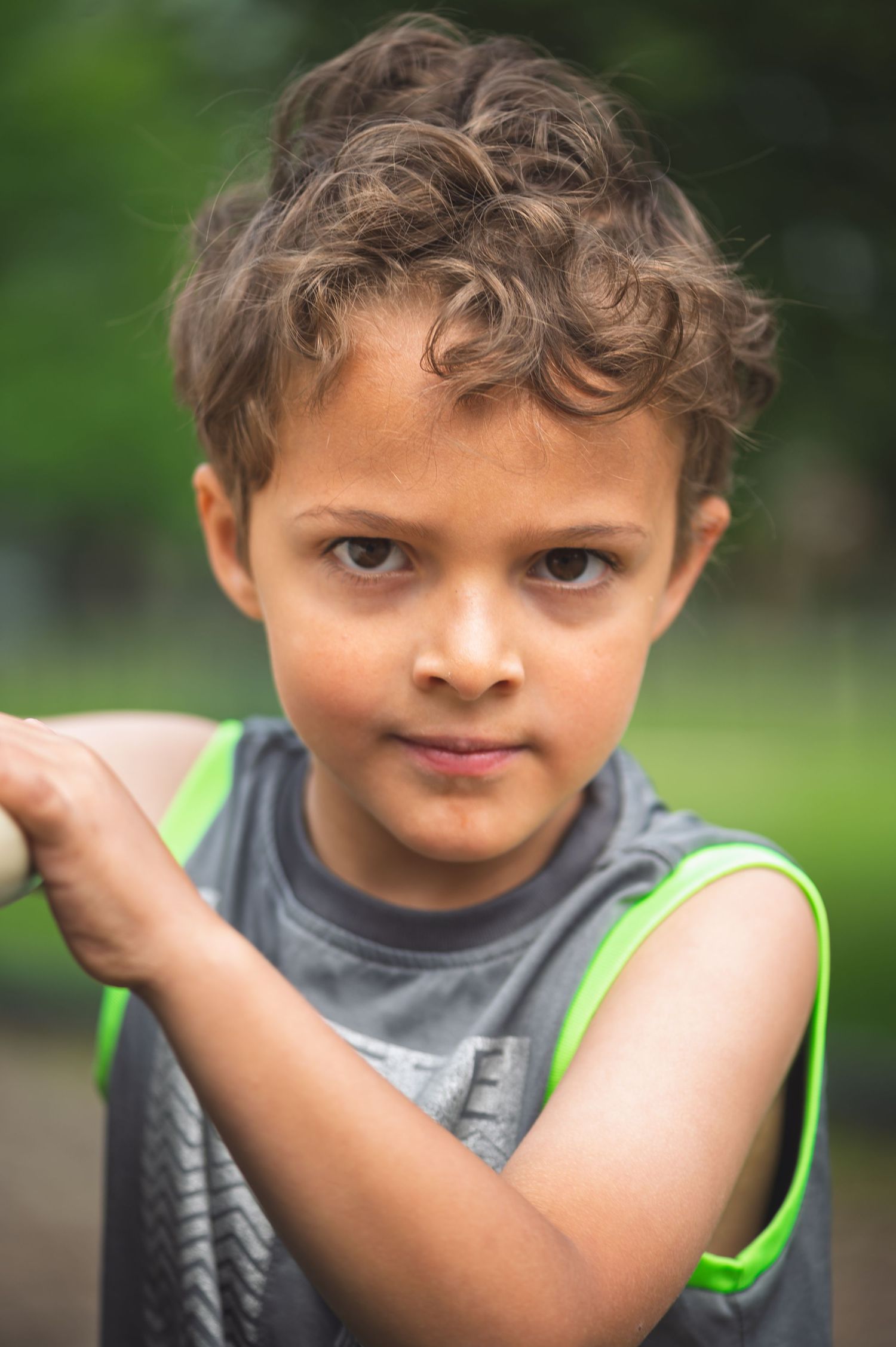 Young child in a gray and green tank top captured in a close-up outdoor portrait with curly hair.