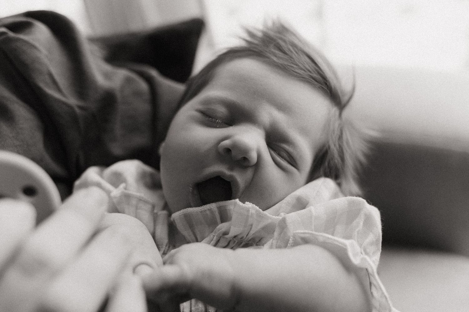 Black and white photo of a sleepy baby yawning while lying down.