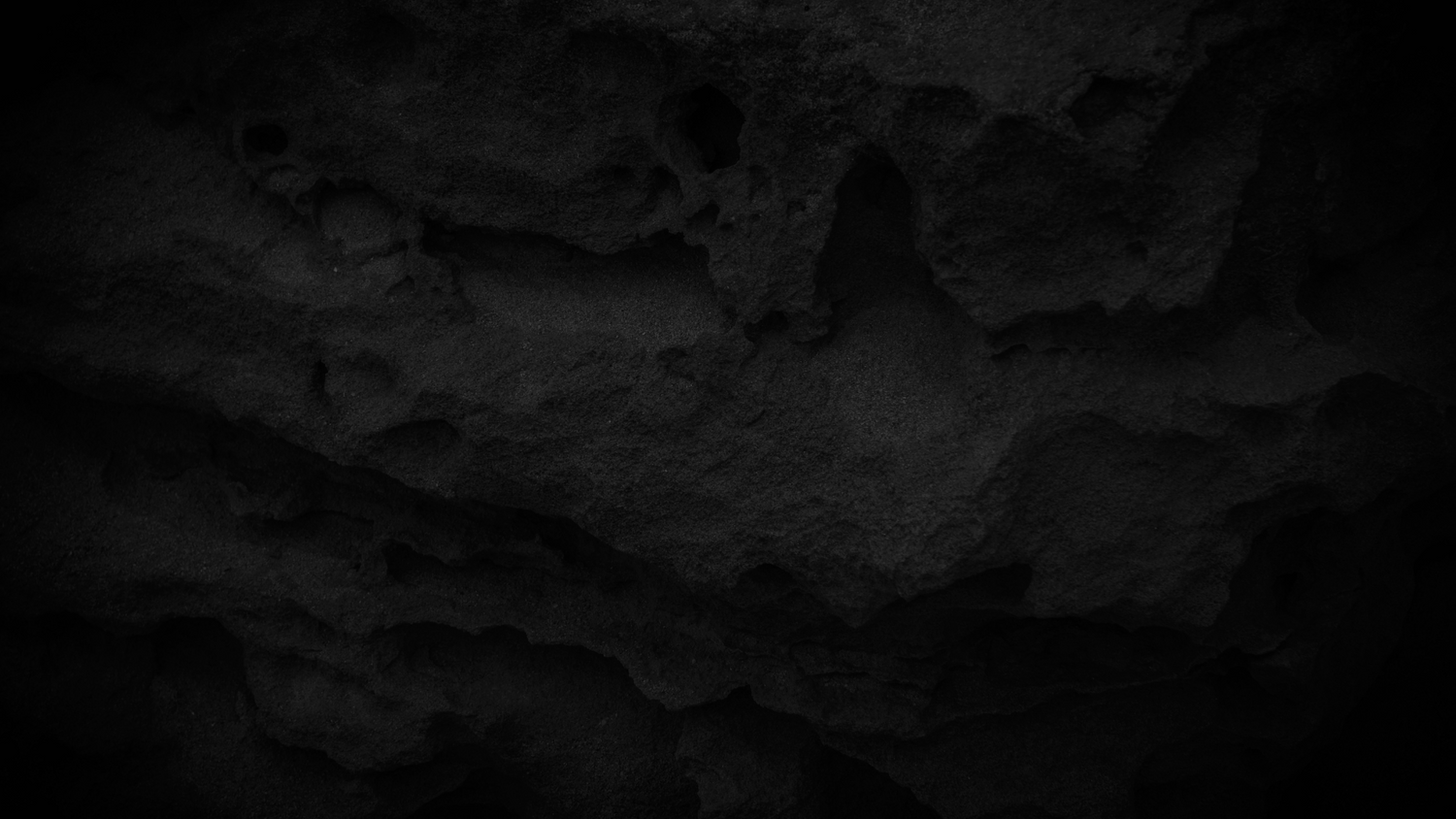 Dark textured background with rough uneven surface in grainy black and charcoal tones.
