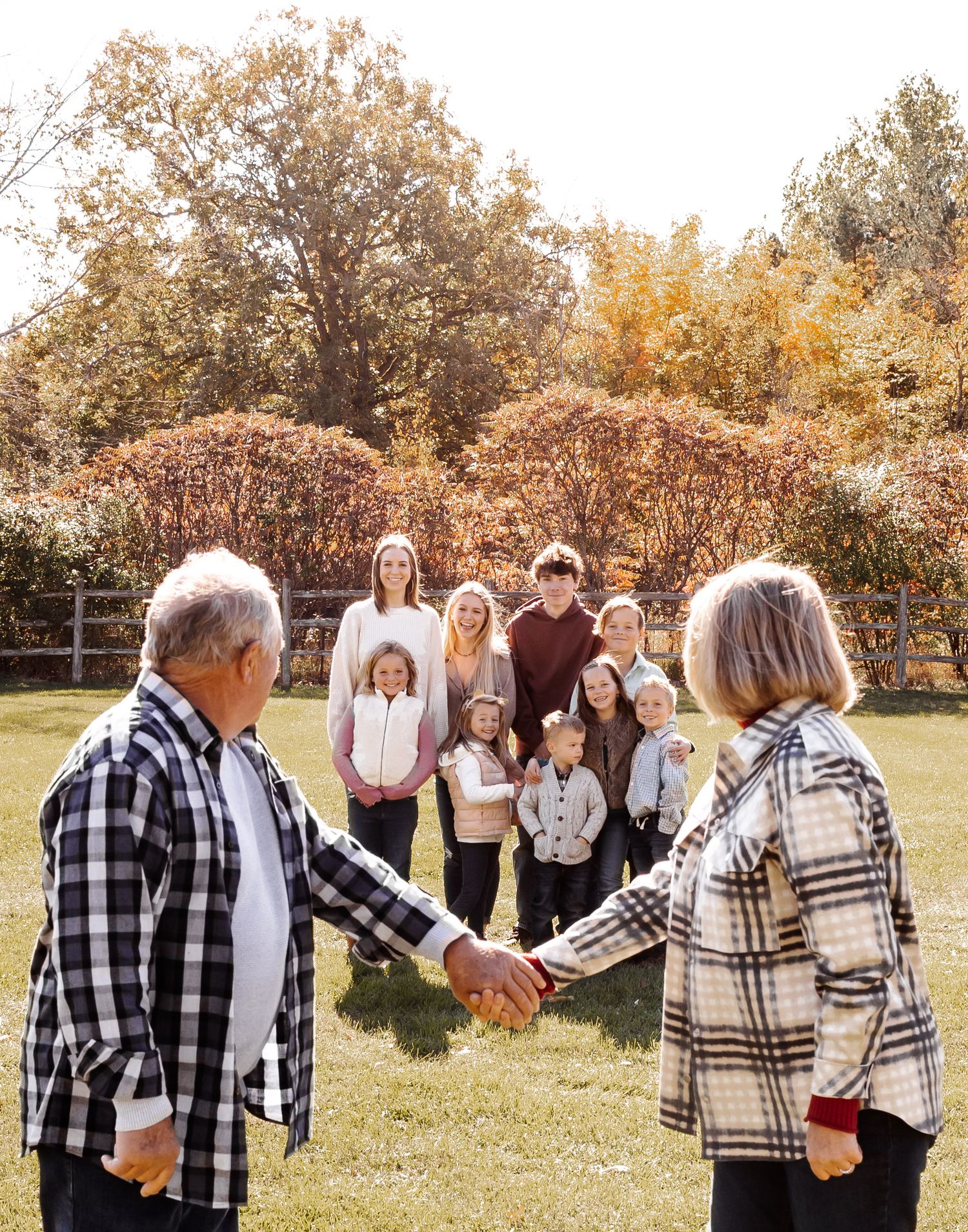 Group of people in plaid and fall attire gather outdoors for autumn family photos in a grassy field.