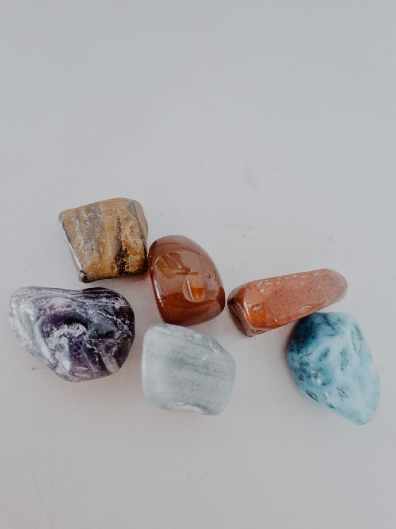 A collection of rough gemstones in purple, blue, and orange hues arranged in a row on a light gray background.