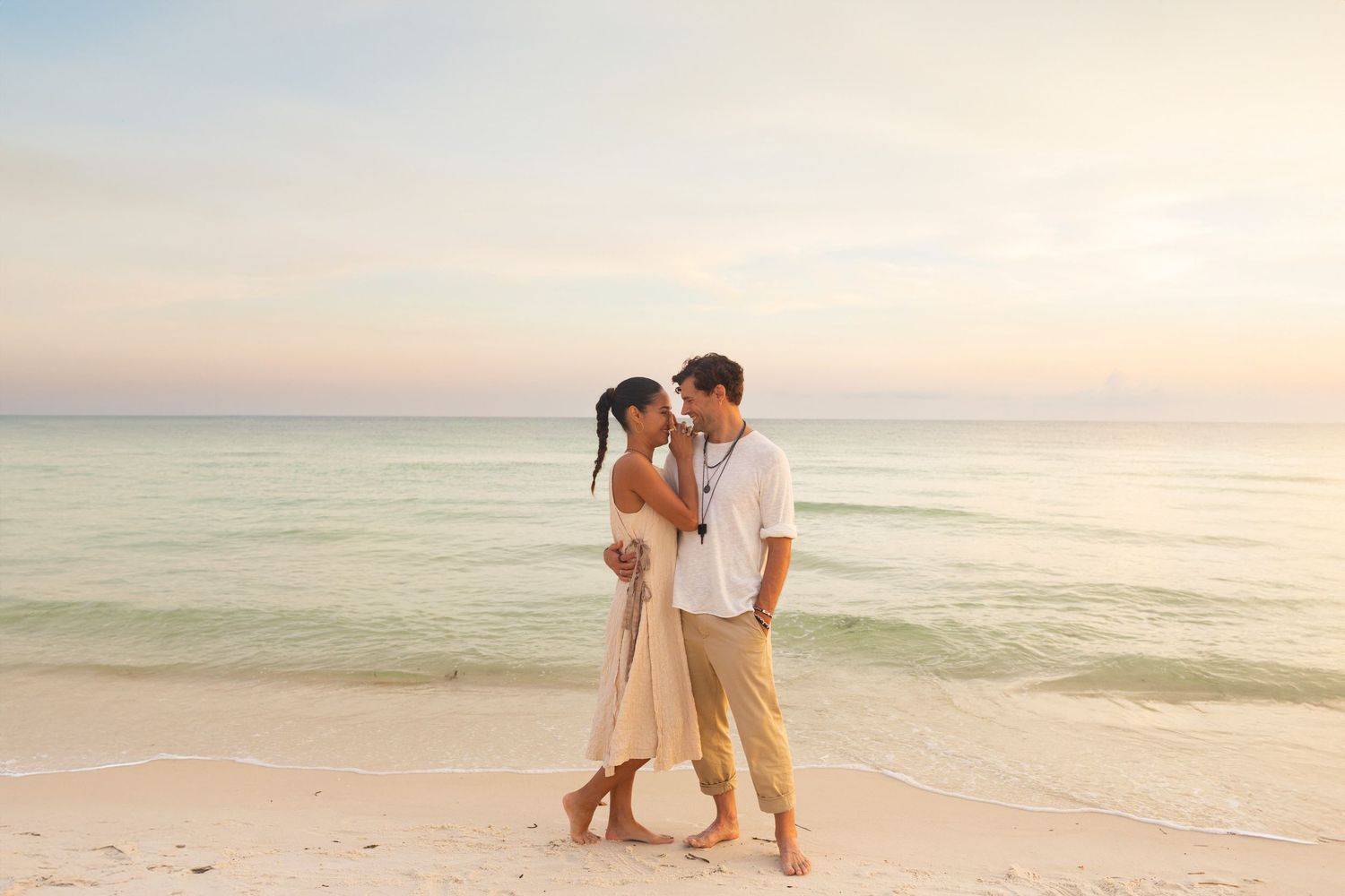 Couple enjoying a romantic sunset stroll along a pristine beach with gentle waves in the background.