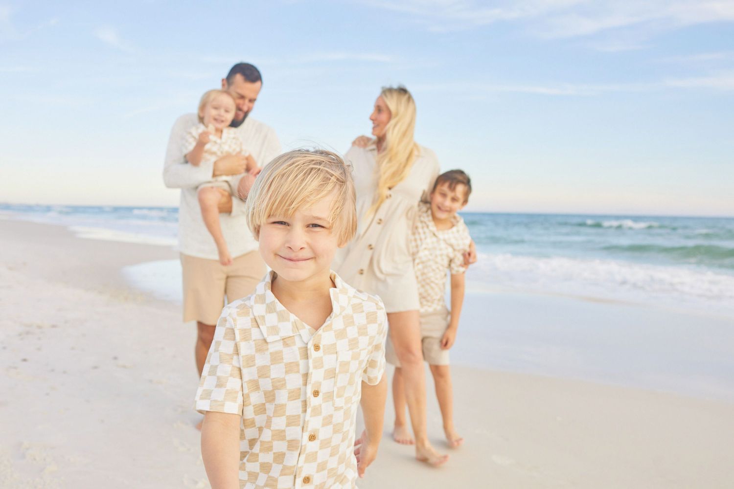 Family enjoying a sunny day together walking along a white sandy beach with ocean waves in the background.