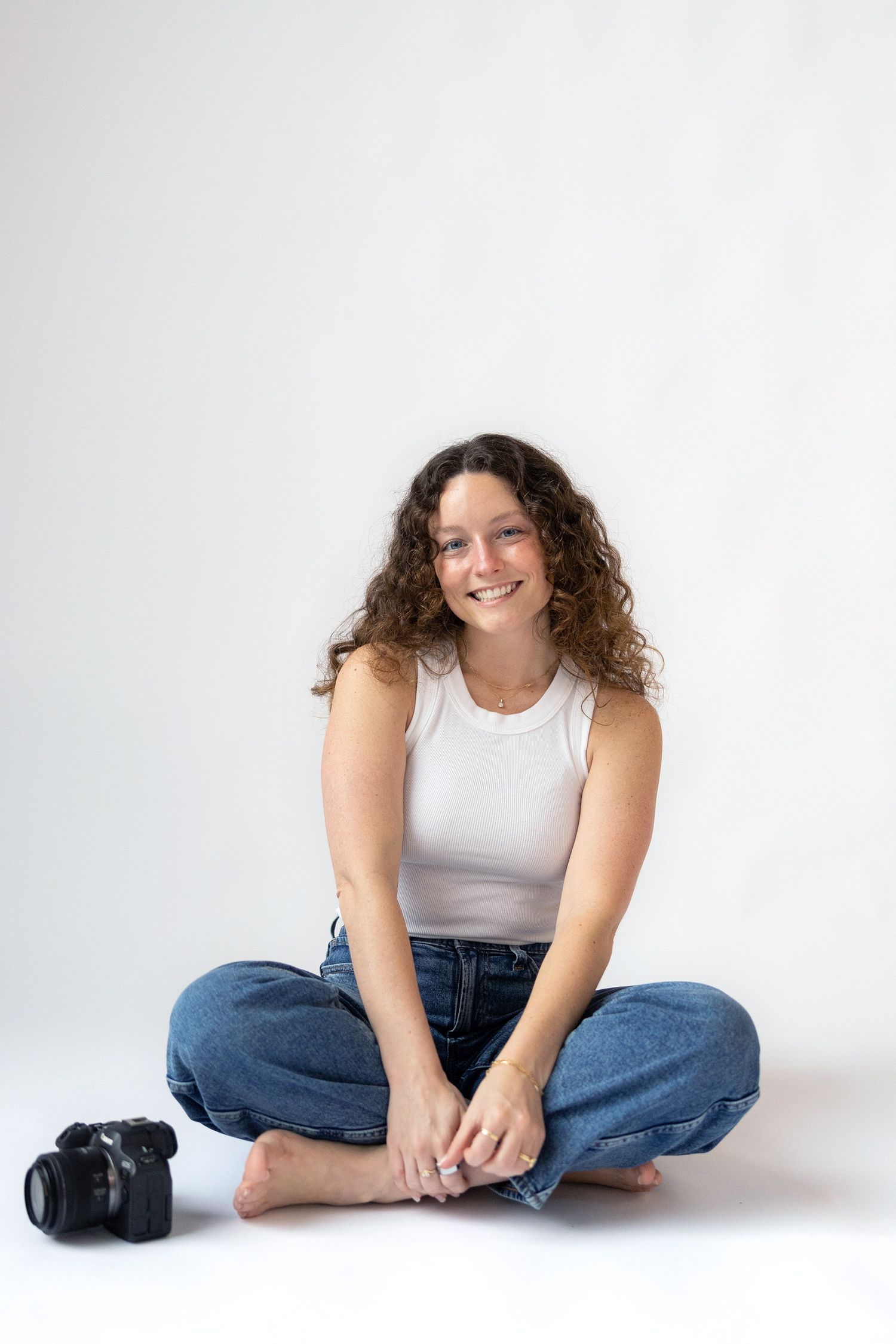 A casual portrait series showing someone in a white tank top and jeans sitting on a white backdrop.
