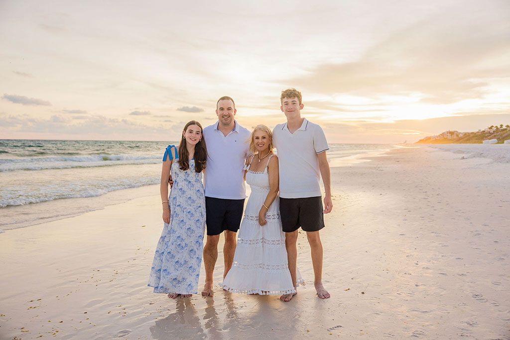 Family walking together on a white sandy beach at sunset with waves crashing in the background.