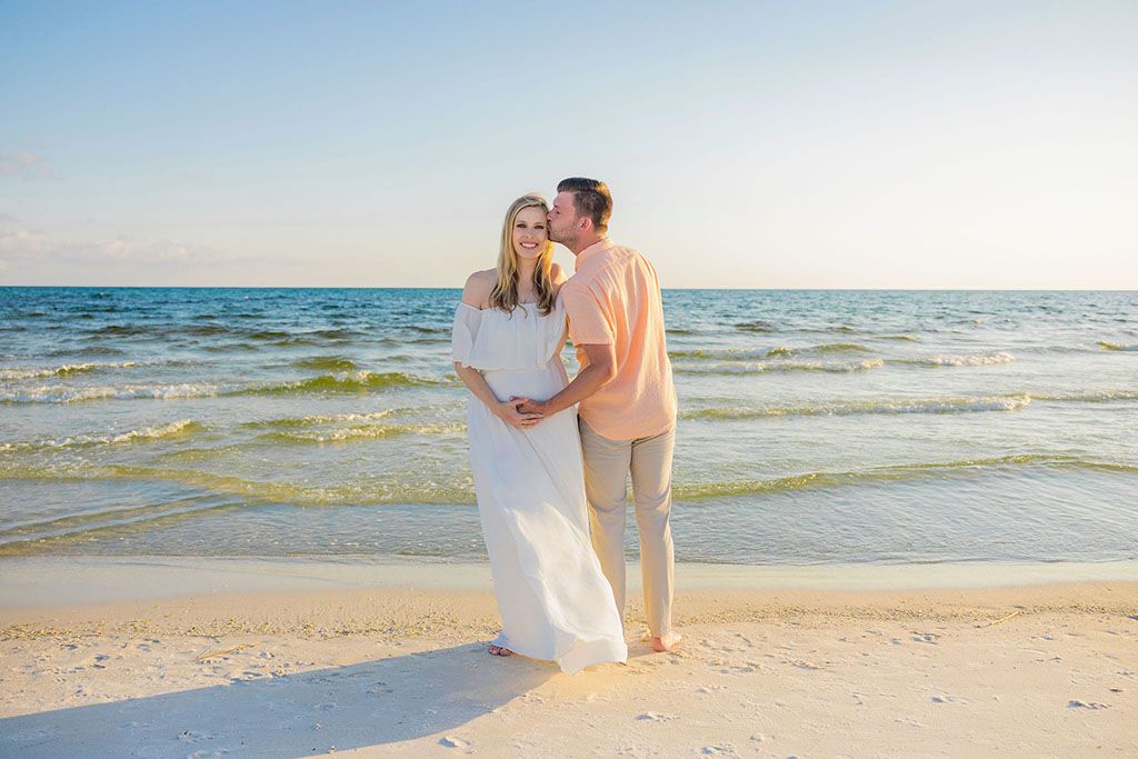 A couple walks hand in hand along a scenic beach shoreline at sunset with waves gently rolling in.