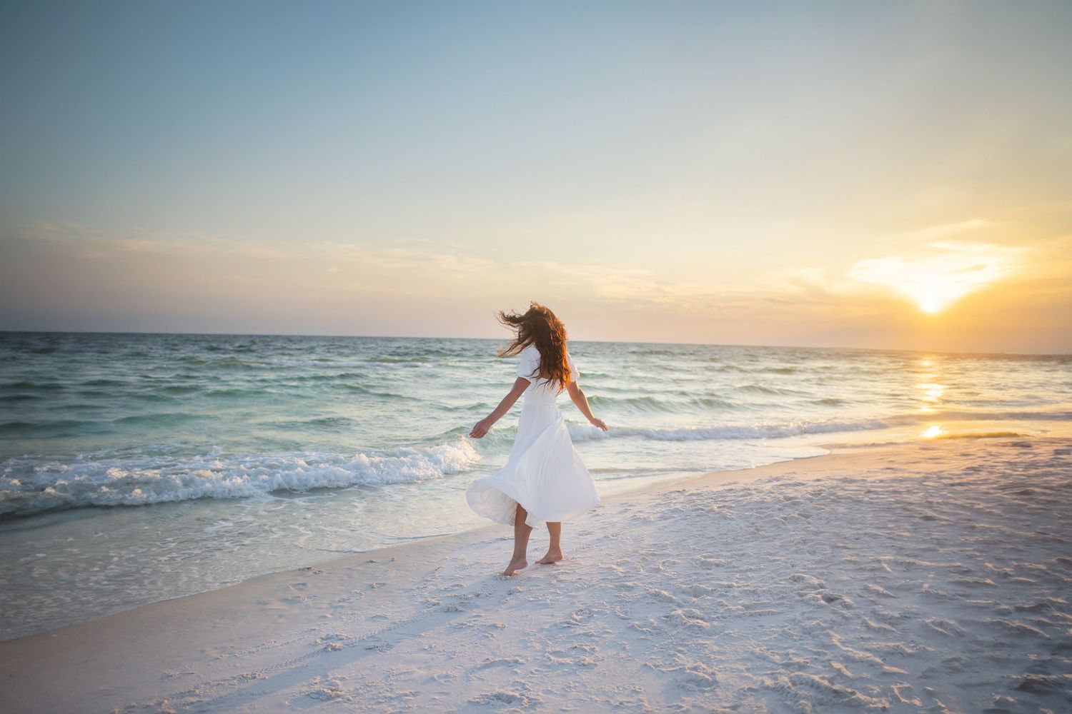 A silhouetted figure walks along a serene beach at sunset with gentle waves lapping at the shore.