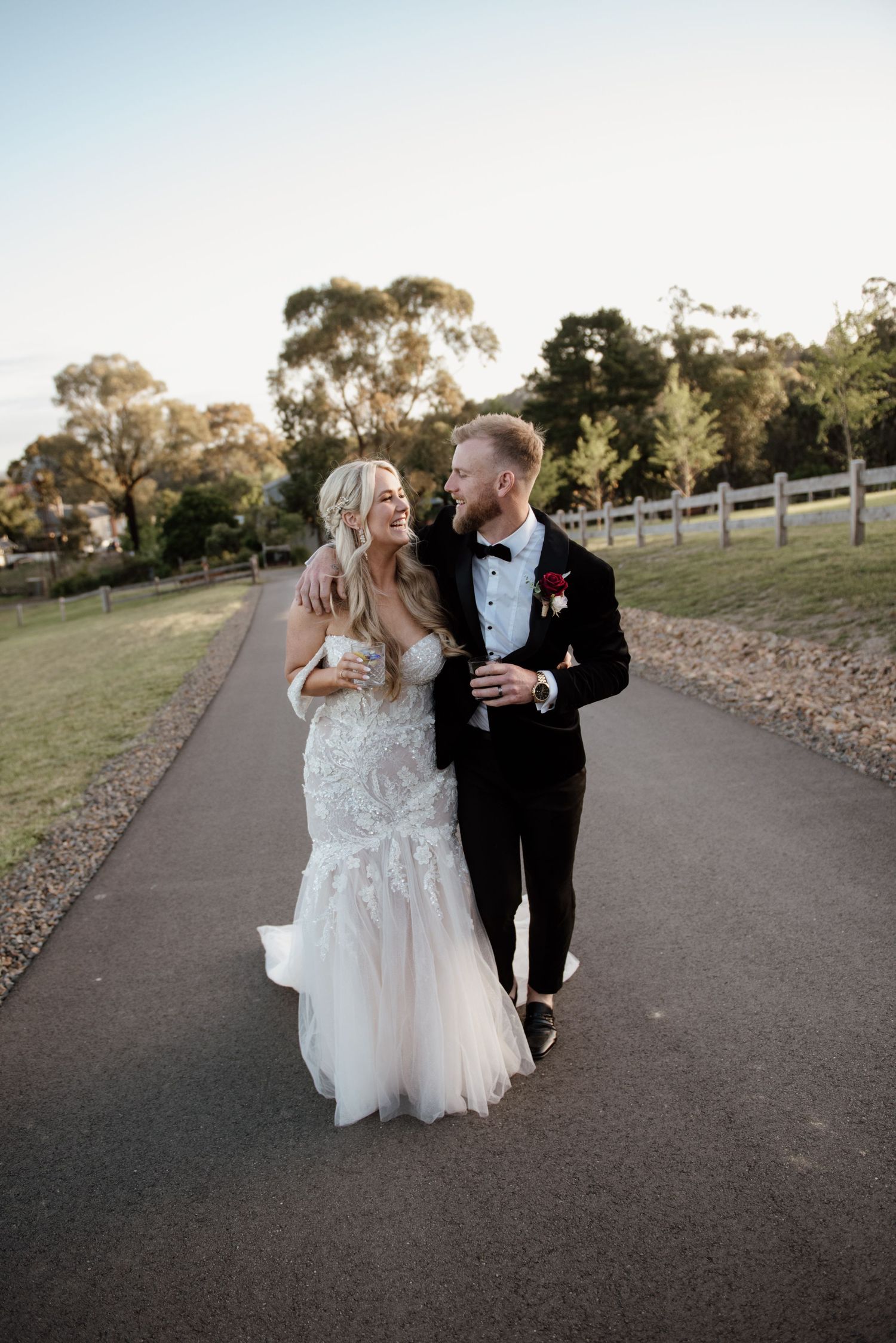 A couple walks along a path sharing drinks during their wedding celebration.