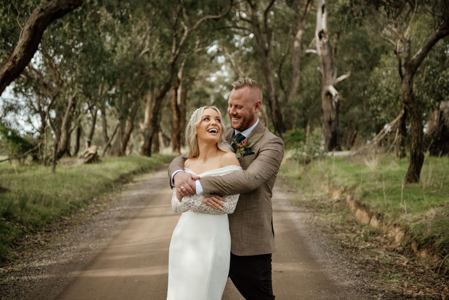 A romantic embrace between newlyweds on a tree-lined country road.