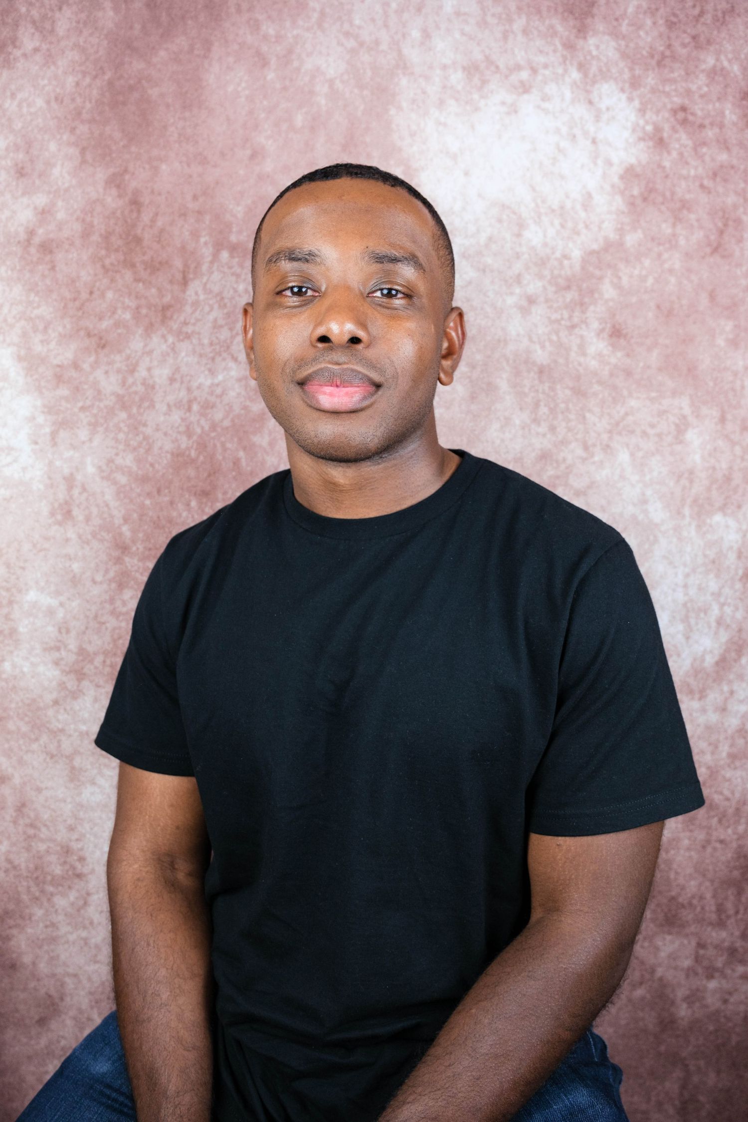 Studio portraits of person in black t-shirt against mottled pink background.