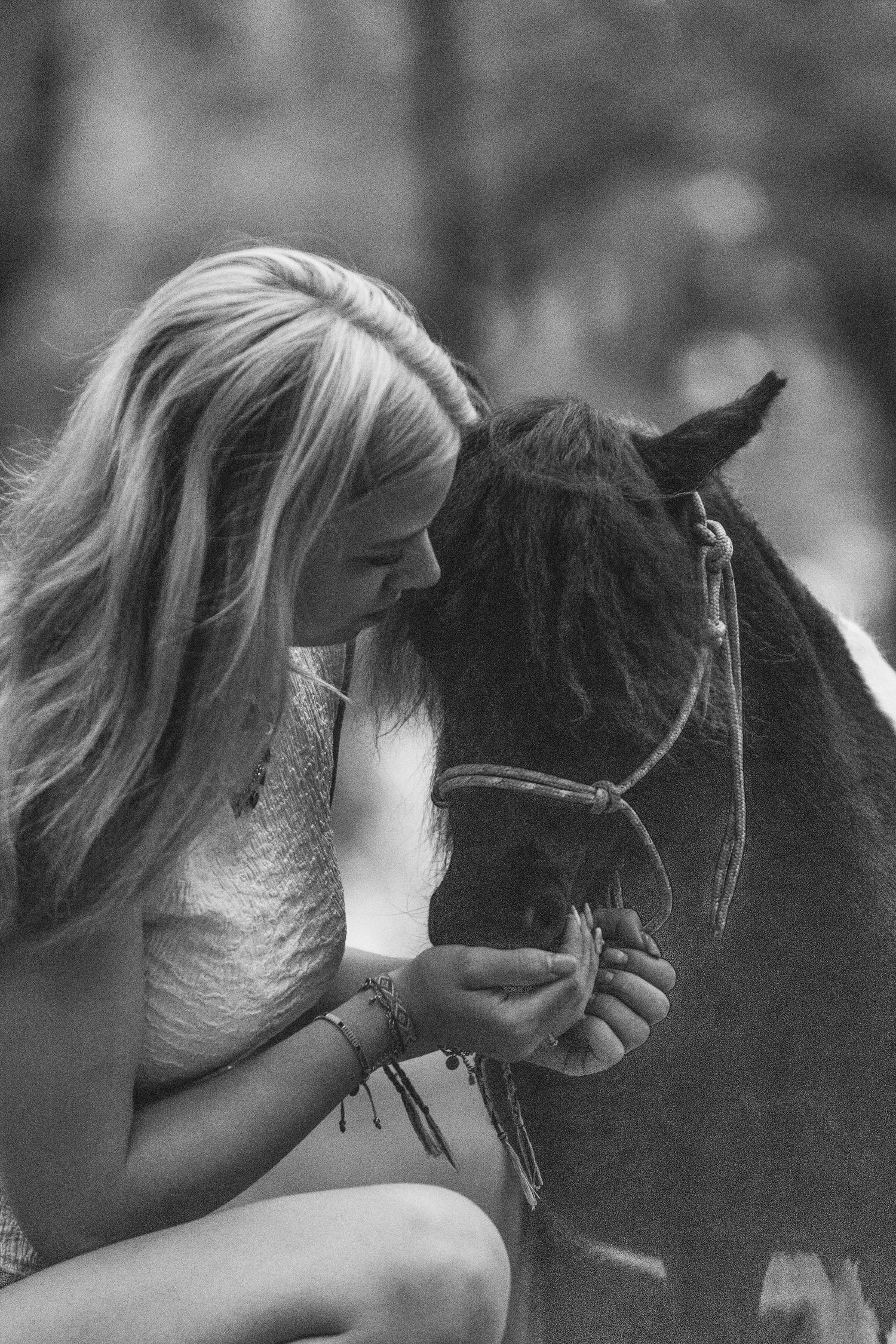 Black and white photo of a blonde woman leaning in close to kiss a small dark horse gently.