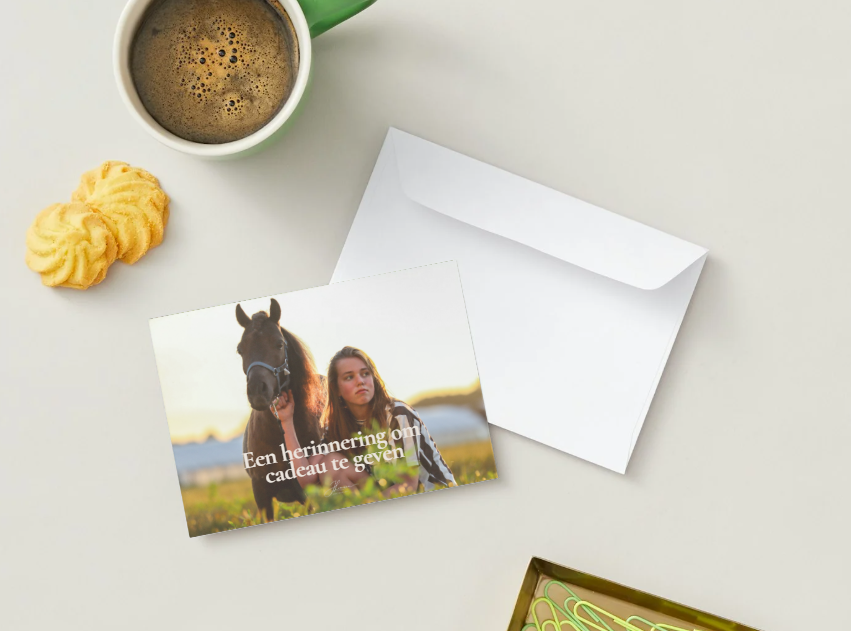 Greeting card featuring a woman with a horse and Dutch text, displayed next to envelope with coffee nearby.
