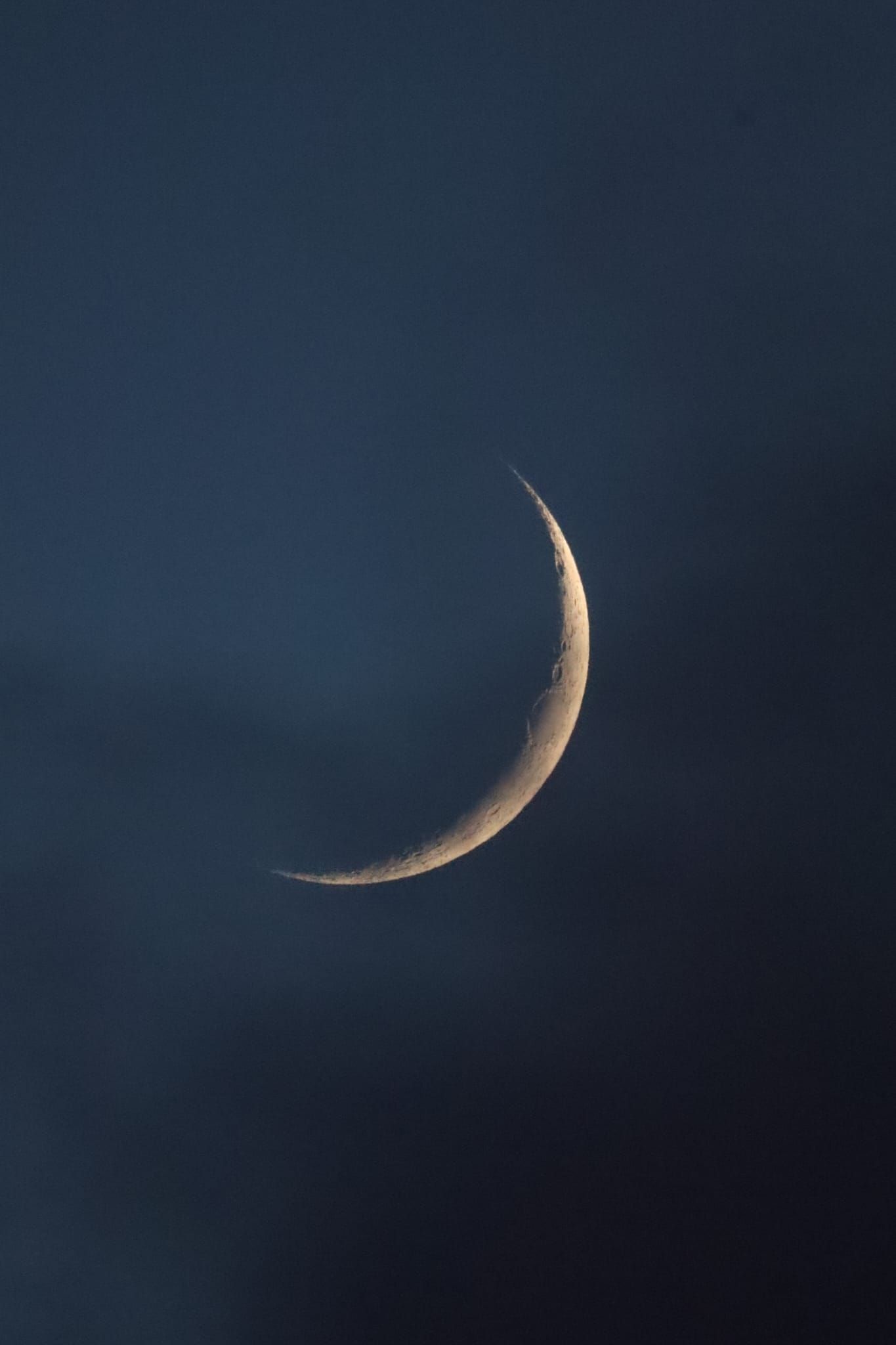 A thin crescent moon glowing golden against a deep blue twilight sky.