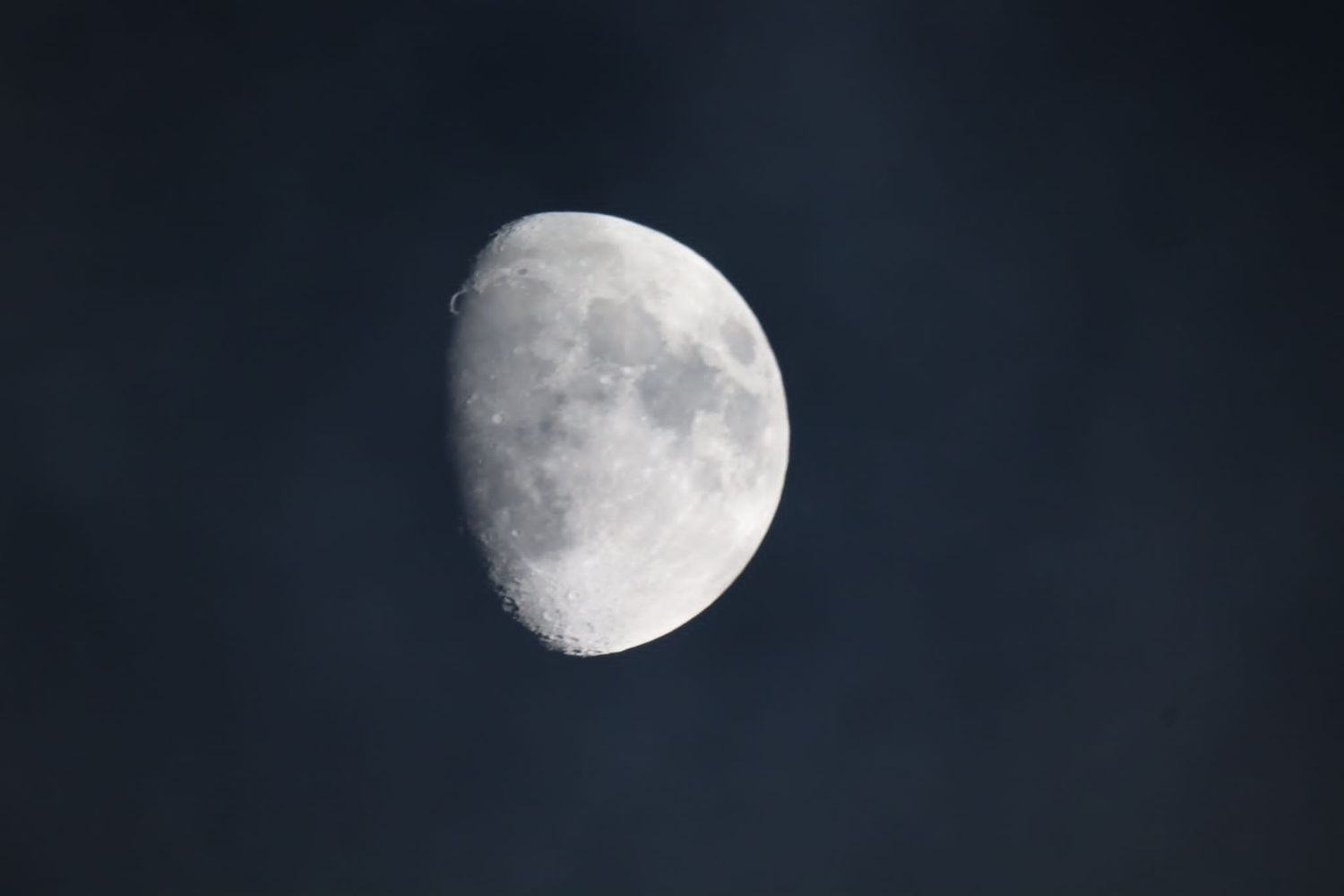 A waxing gibbous moon with visible craters against a deep blue cloudy night sky.