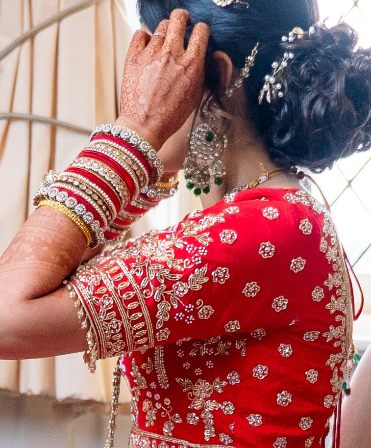 Close-up of Indian bride in red embroidered blouse adjusting hair with mehndi hands and bangles.