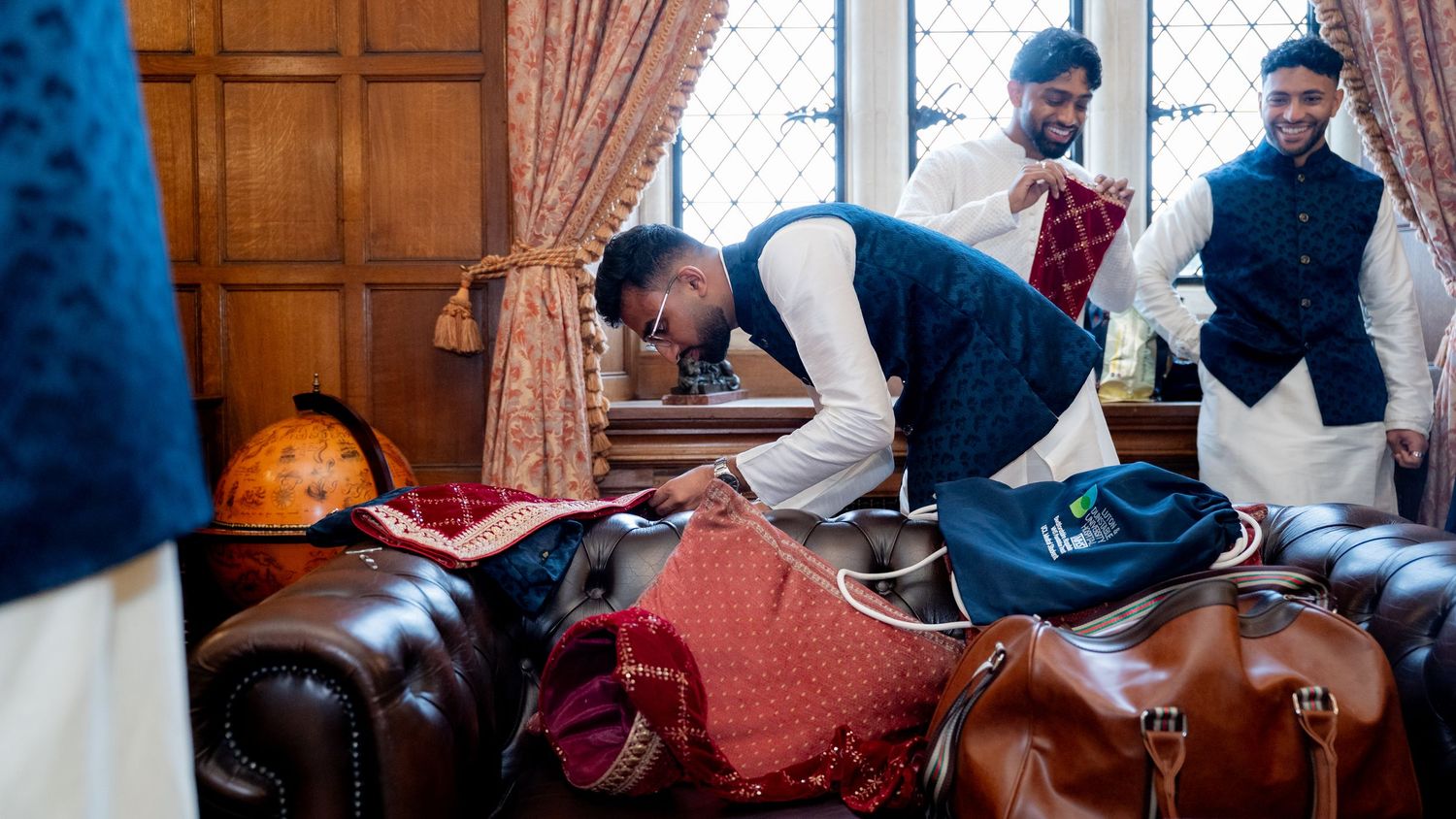 Indian groom and groomsmen in traditional kurta preparing wedding accessories on a leather sofa.