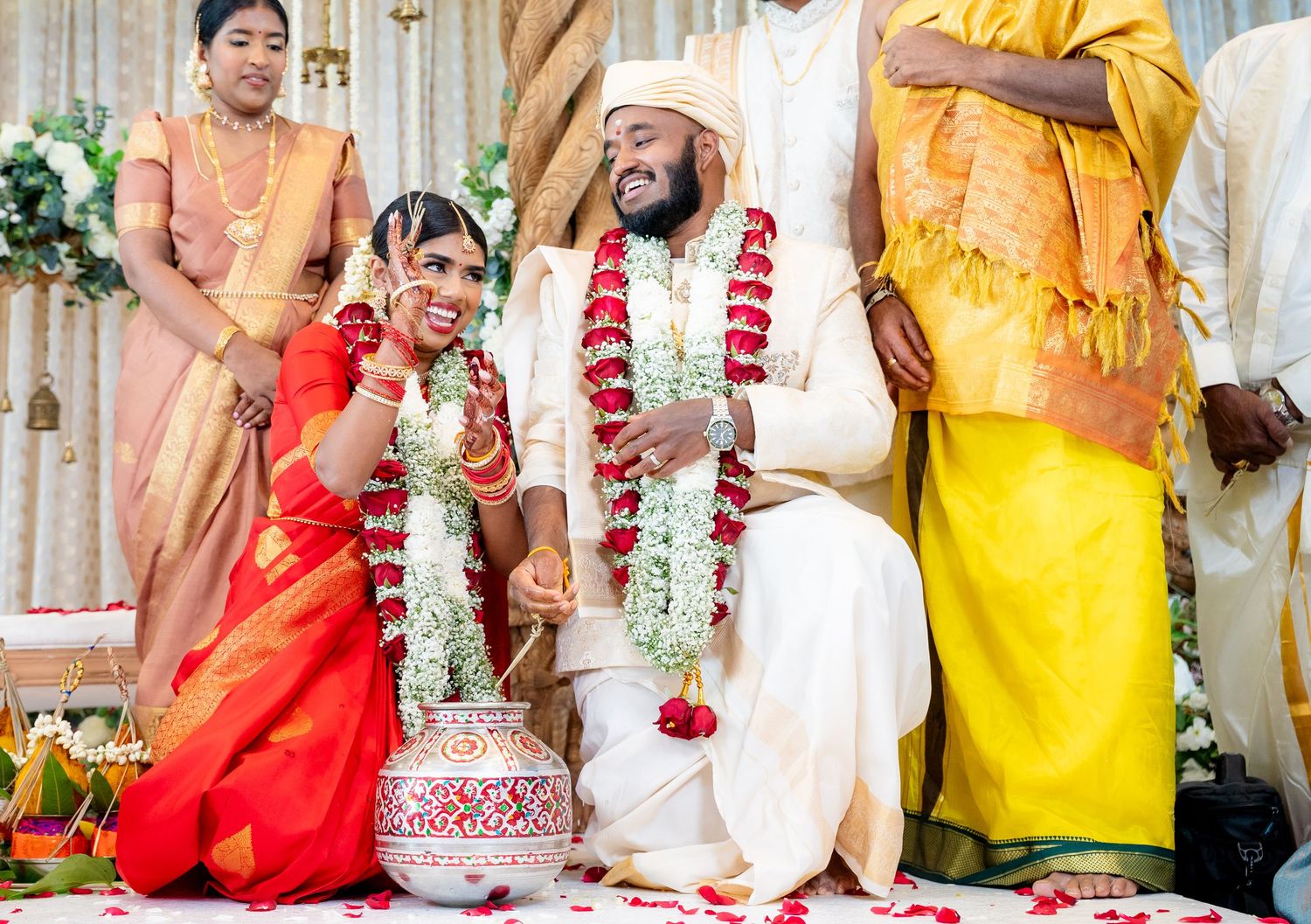 A joyful Indian couple in traditional wedding attire with floral garlands, seated during a colorful Hindu wedding ceremony.