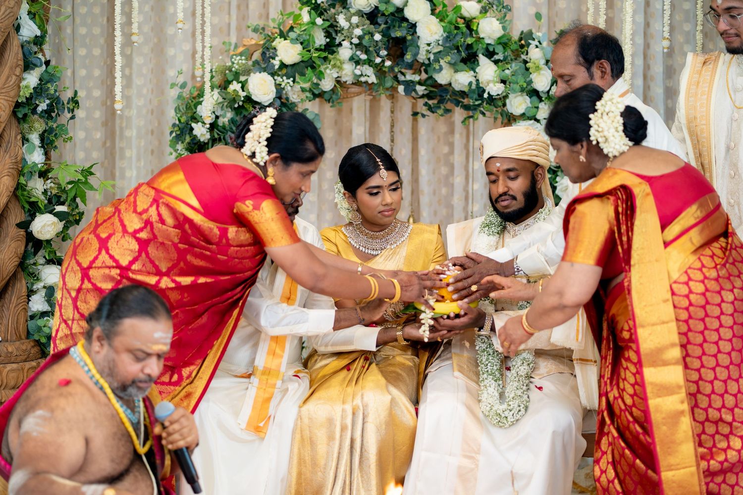 South Indian wedding ceremony with family members performing traditional rituals for bride and groom at mandap.