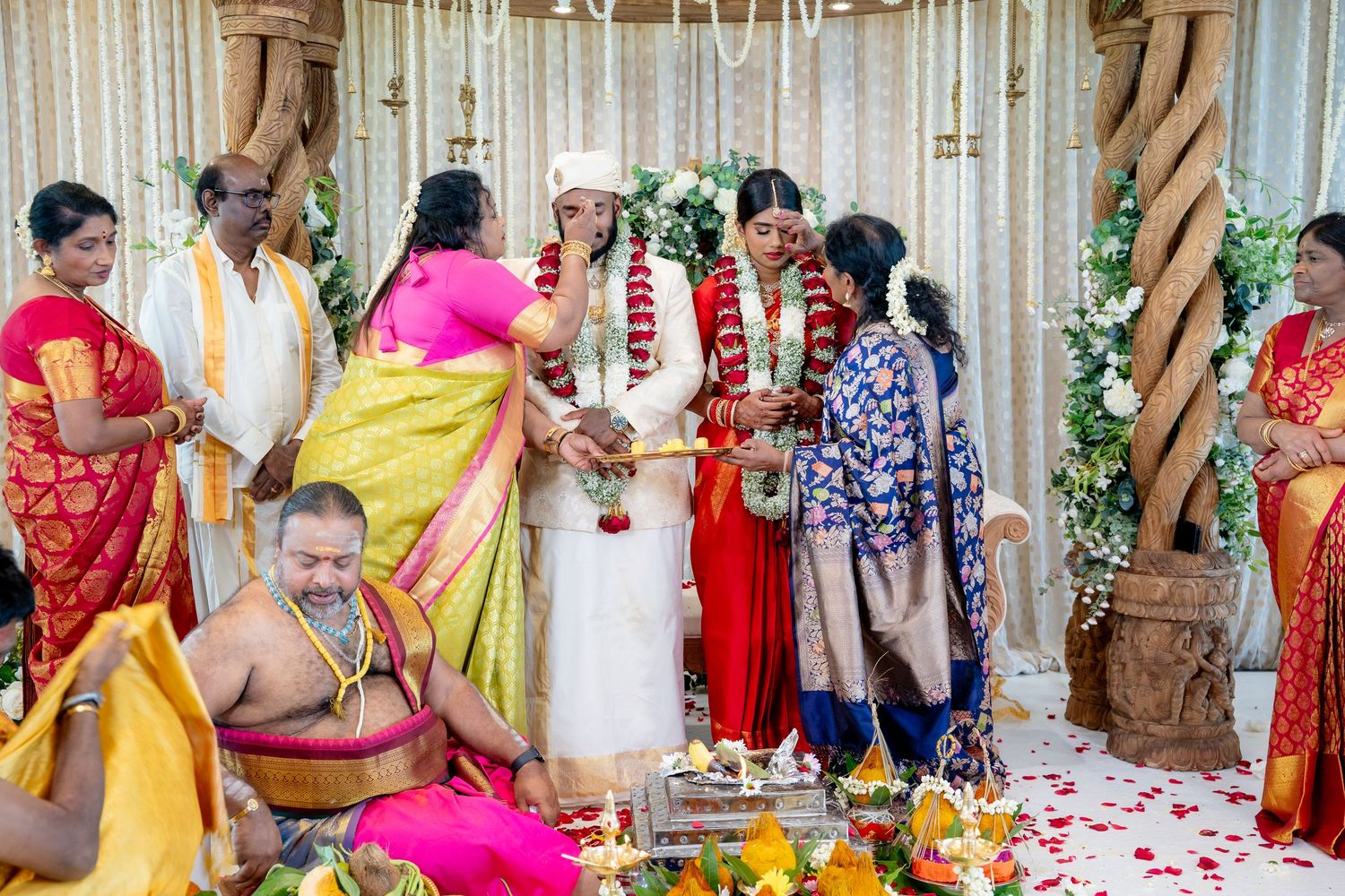Traditional Telugu wedding rituals with priest performing ceremony as bride and groom exchange garlands amid family.