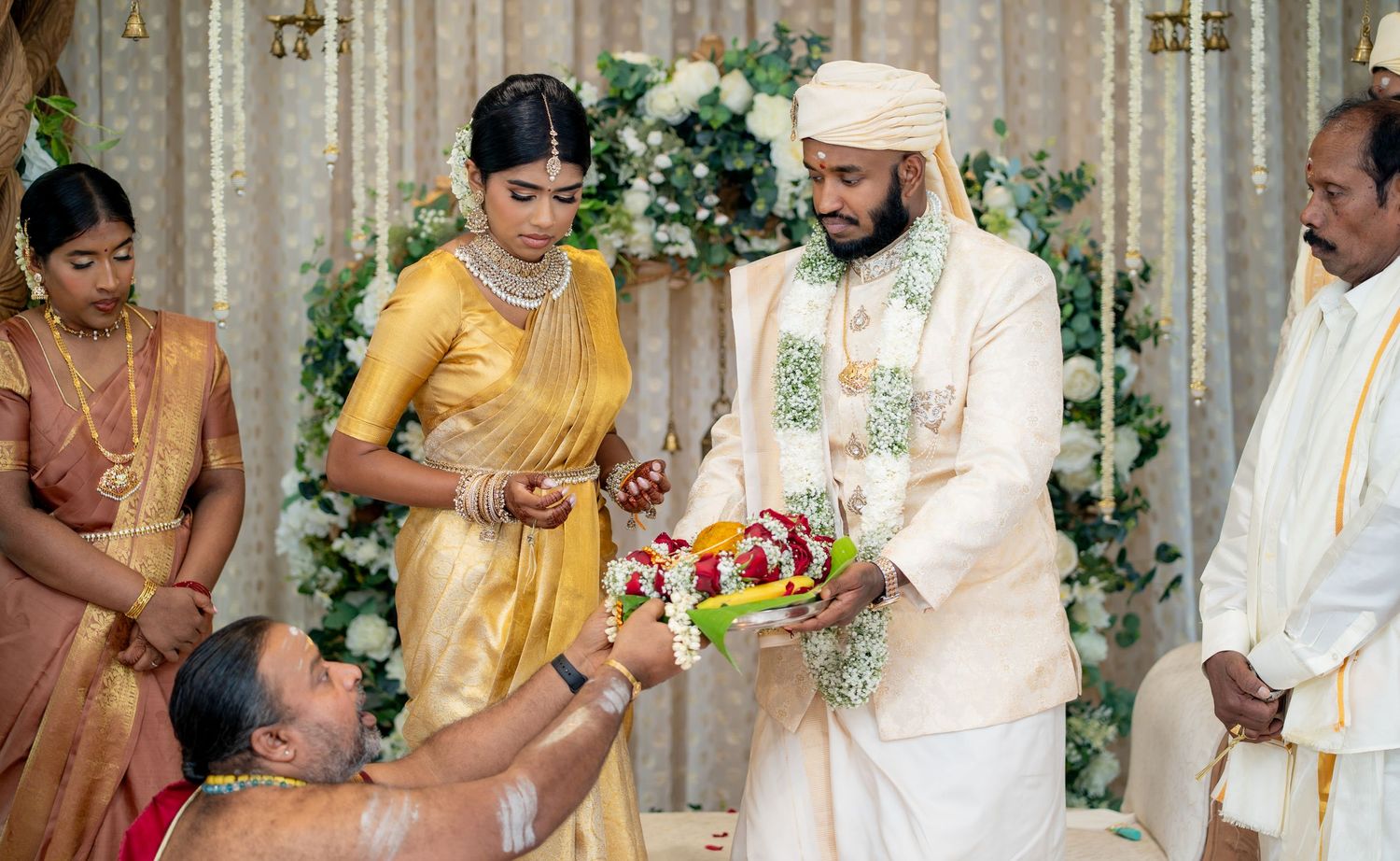 Traditional Indian wedding ceremony with bride in yellow saree and groom in white attire exchanging floral garland.