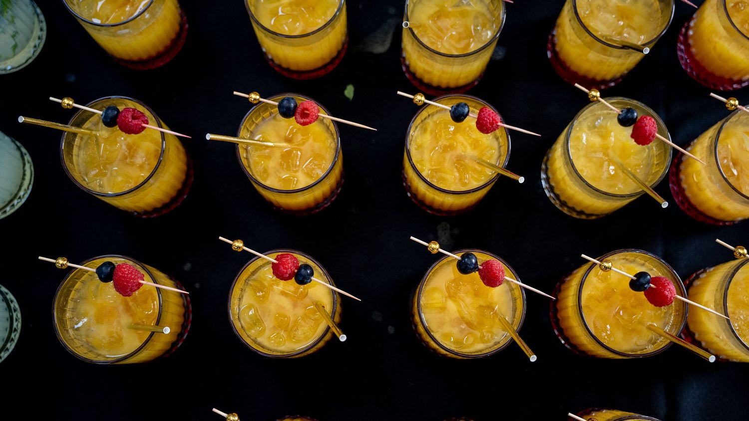 Overhead view of rows of orange mango cocktails garnished with berries on skewers.