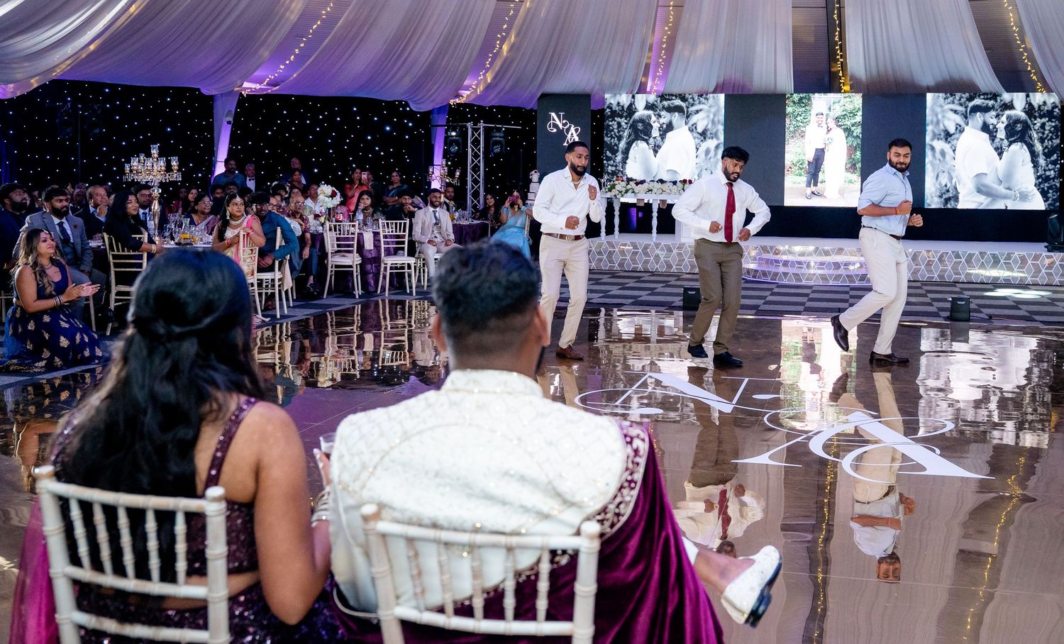 Guests seated at tables watching a wedding performance on a shiny dance floor at Indian reception.
