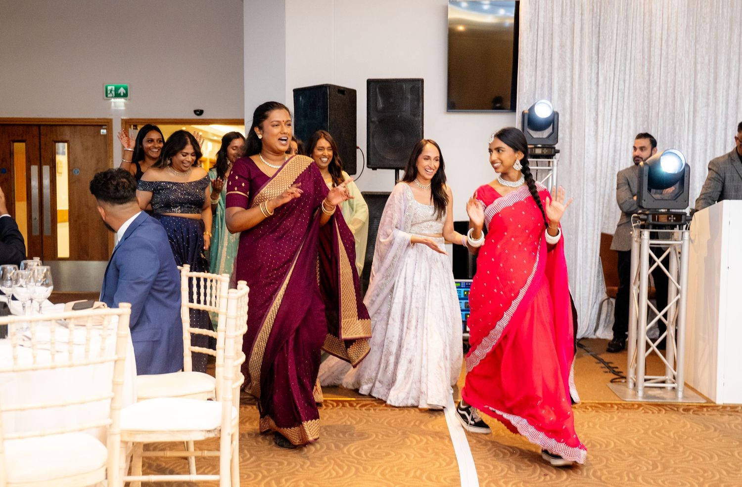 Women in colorful sarees performing a traditional dance at an Indian wedding reception.