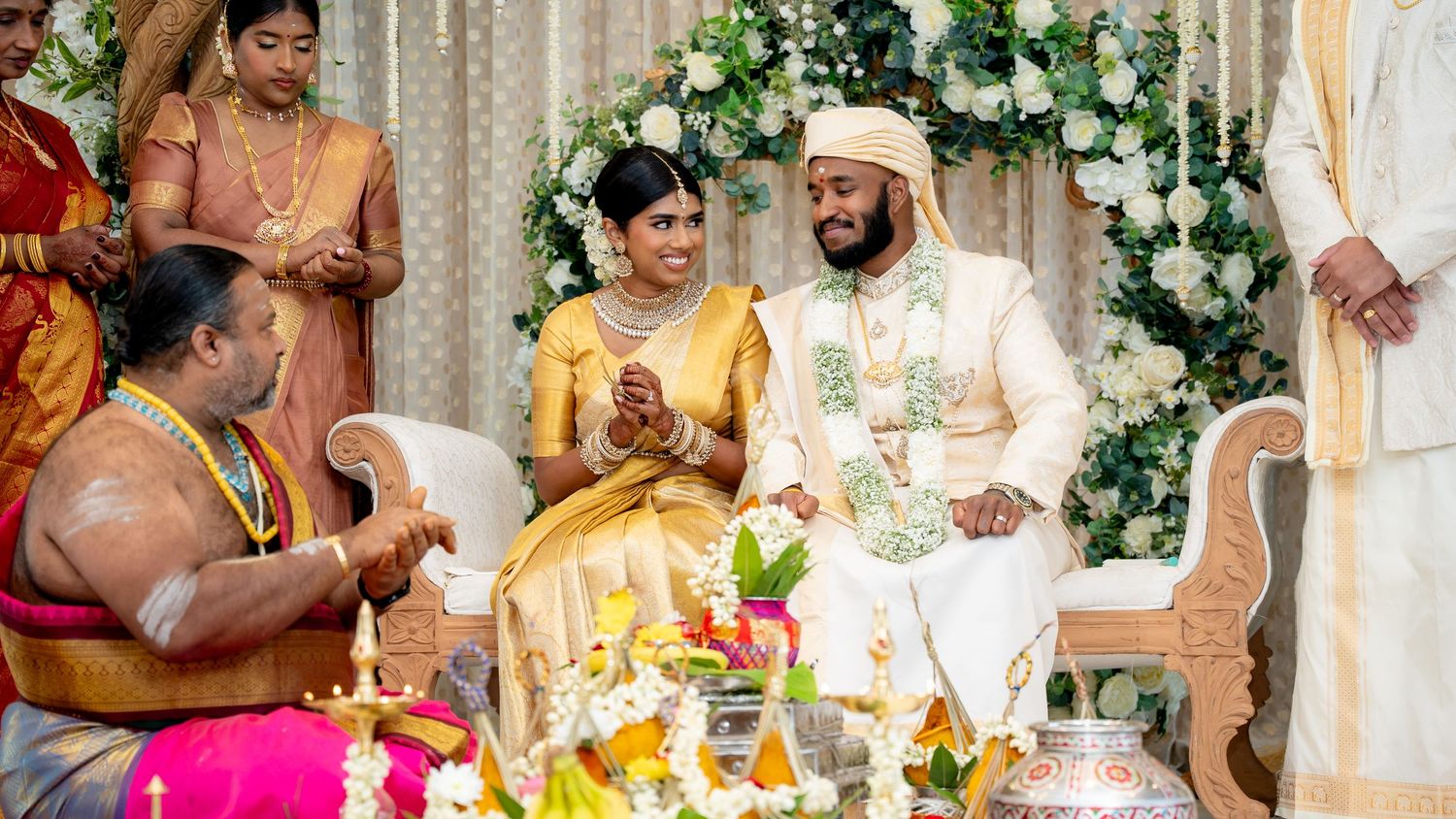 Traditional Indian wedding ceremony with bride and groom in ornate gold and white attire surrounded by family members.
