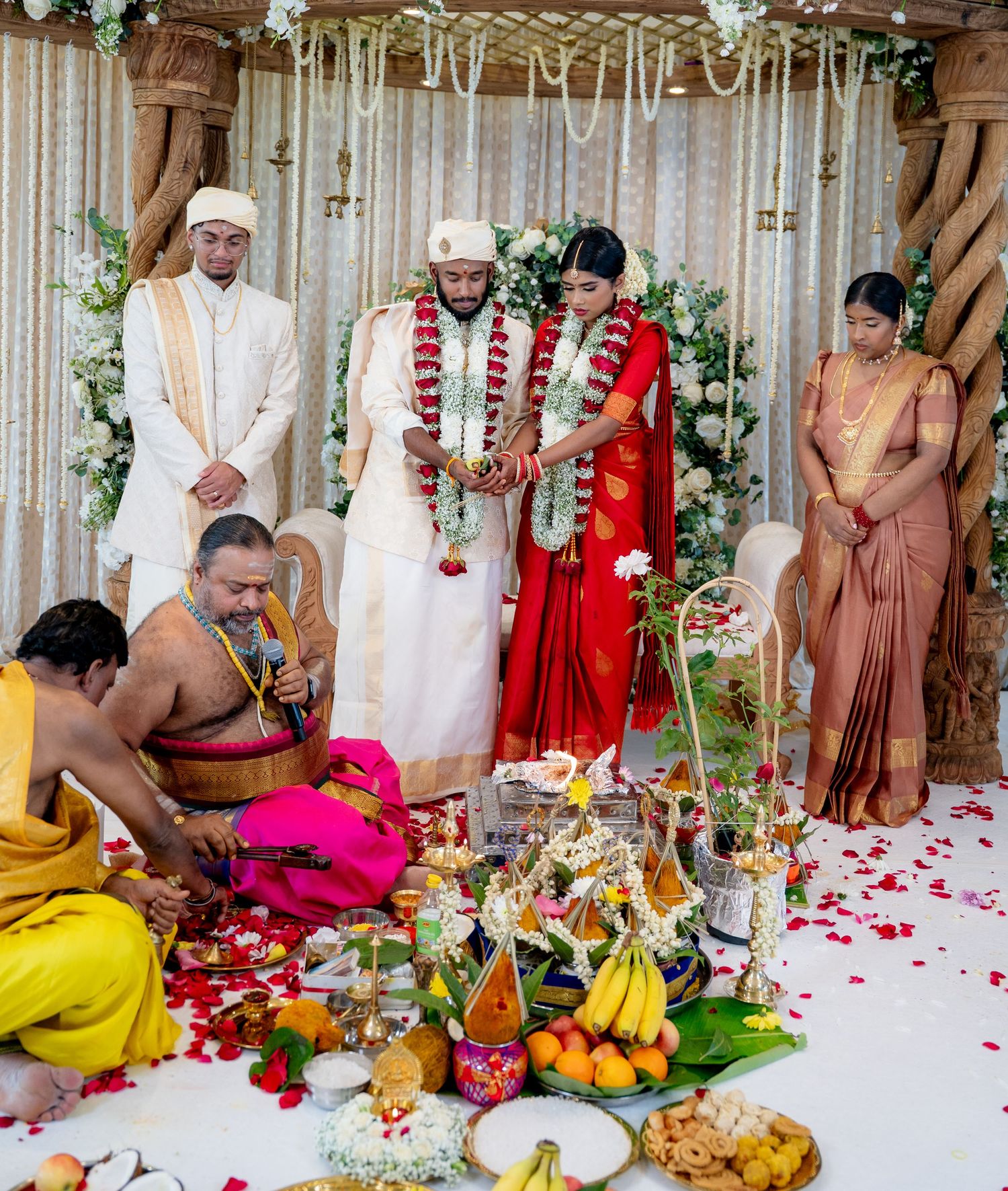 Traditional Hindu wedding ceremony with bride in red saree and groom exchanging garlands at decorated altar.