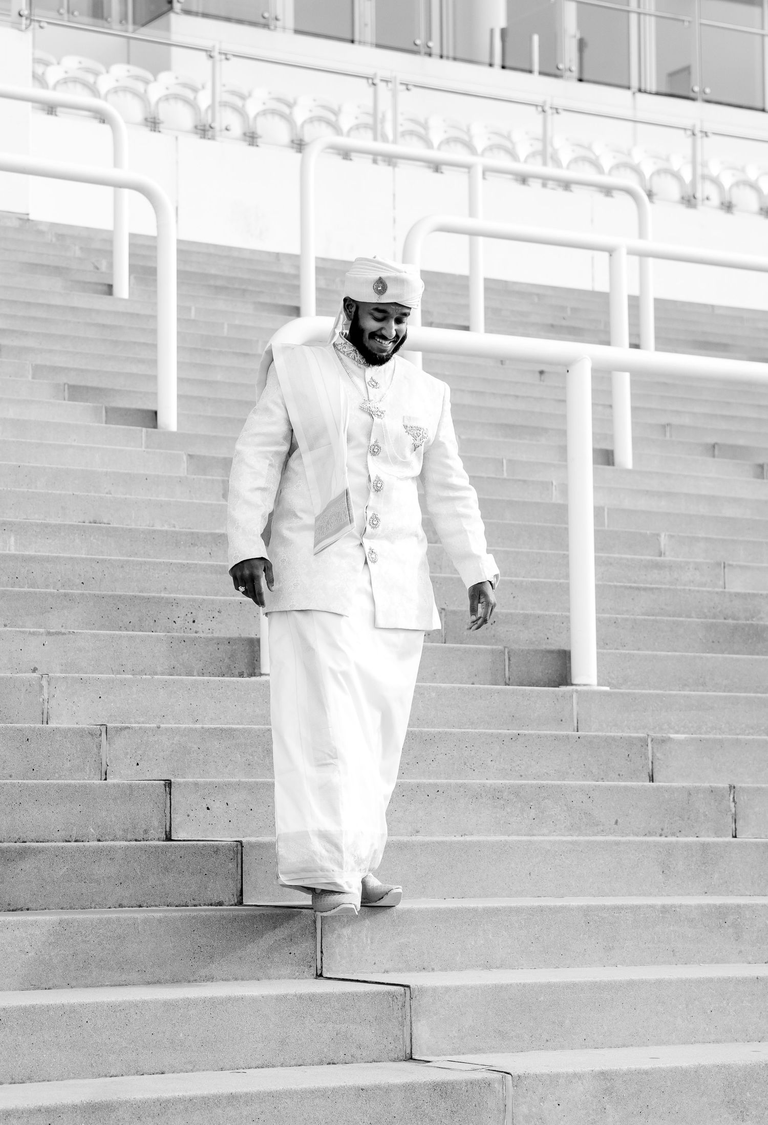 Black and white photo of a man in traditional white attire walking down concrete stadium steps.