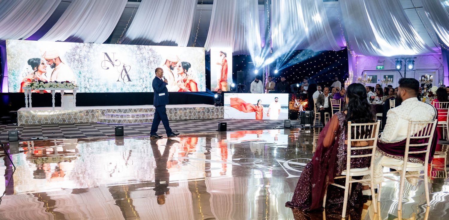 Elegant event venue with dance floor, large display screen, white draping, and guests seated at a formal gala celebration.