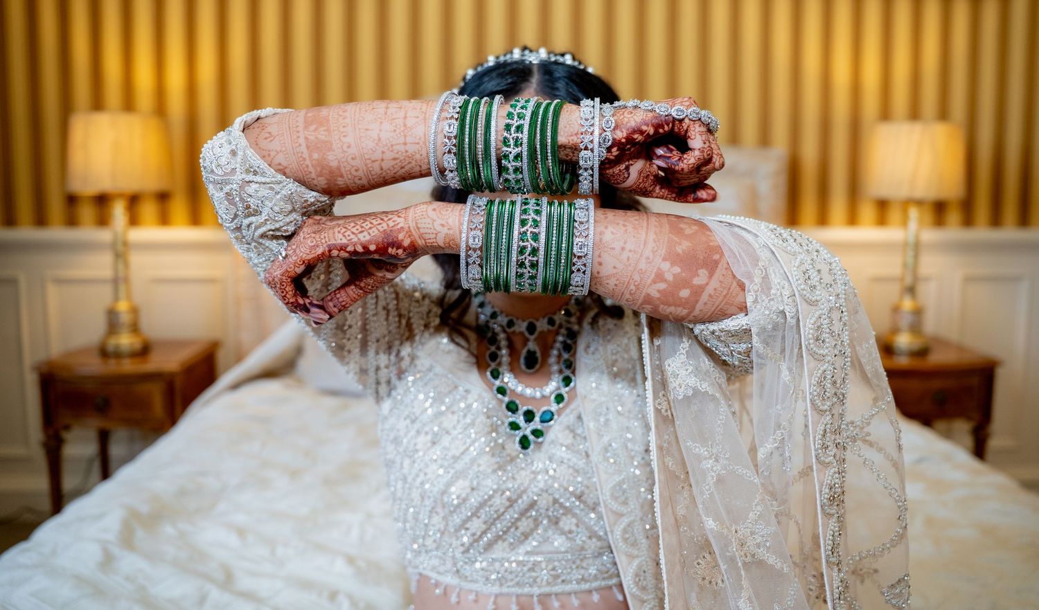 Indian bride adjusting veil showcasing intricate mehndi and green wedding bangles.