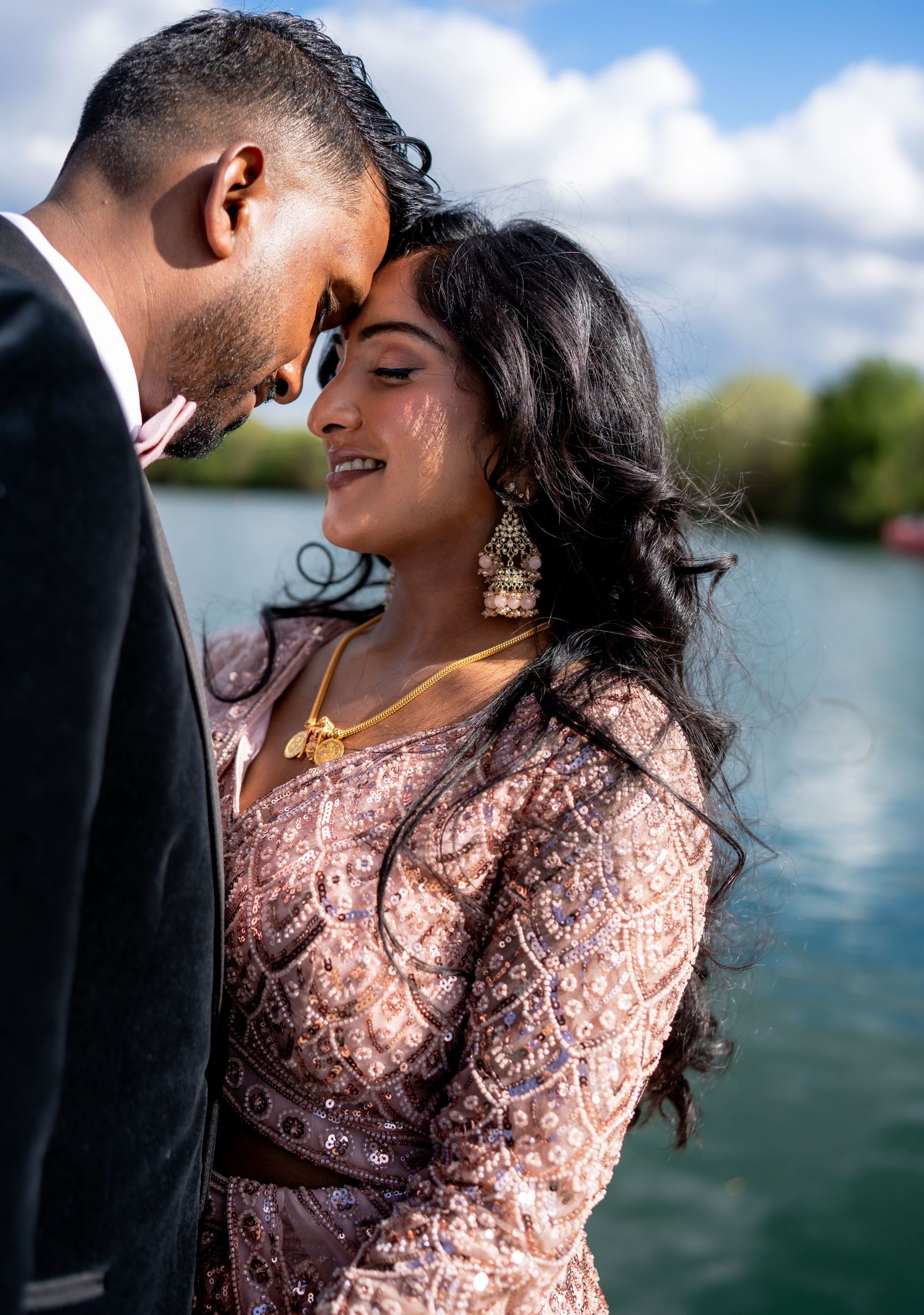 Indian bride and groom touch foreheads intimately by a lake on their wedding day.