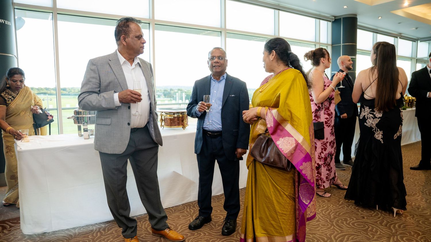 Guests in formal and traditional Indian attire engaged in conversation at a wedding reception.