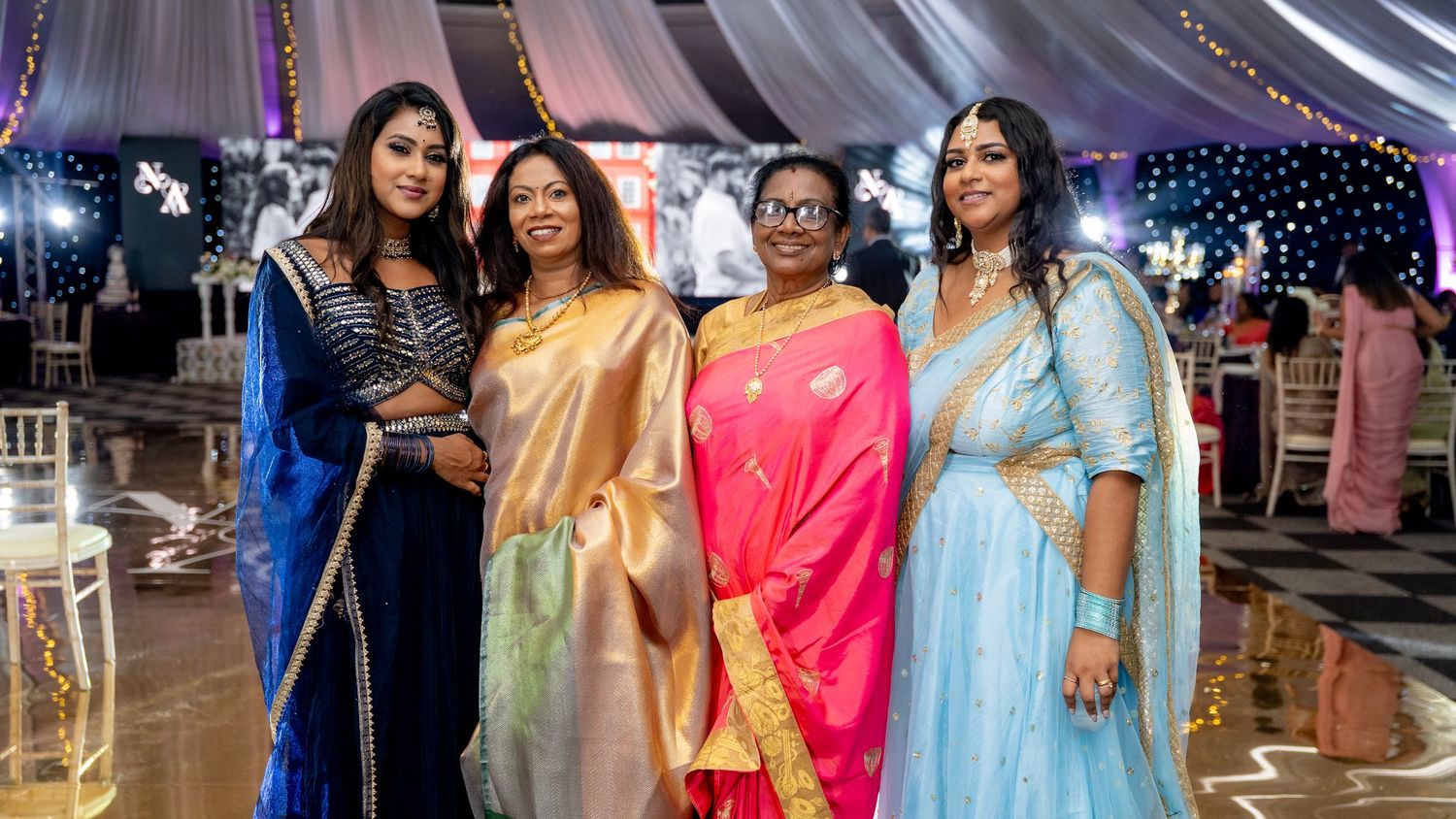 Four women in colorful Indian sarees posing together at a wedding reception.