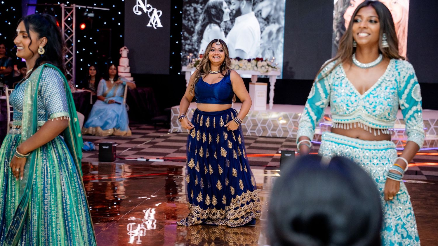 Three women in vibrant traditional Indian lehengas performing at an elegant wedding reception event.