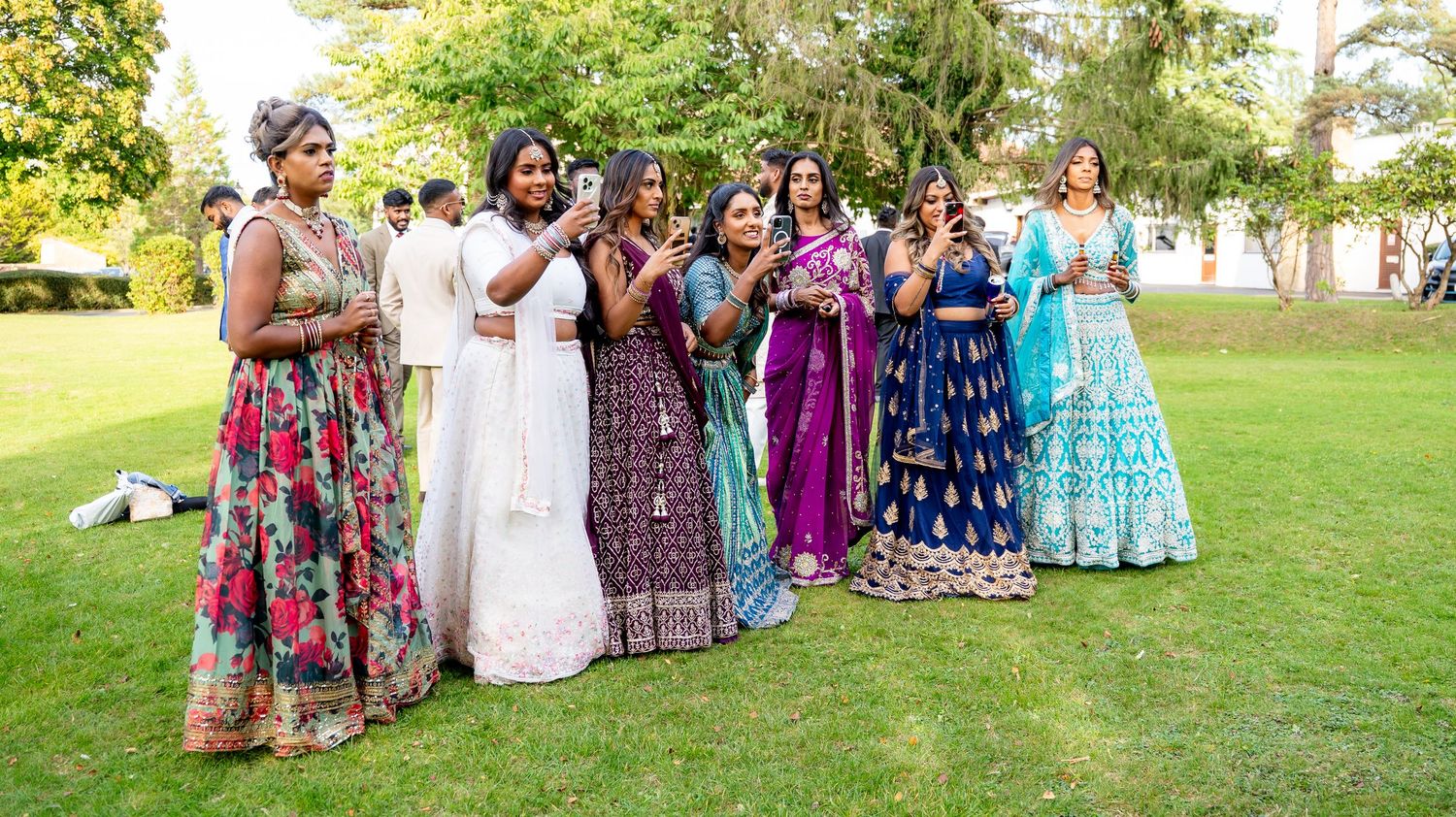 Group of women in colorful traditional South Asian attire gathered on a lawn at a wedding.