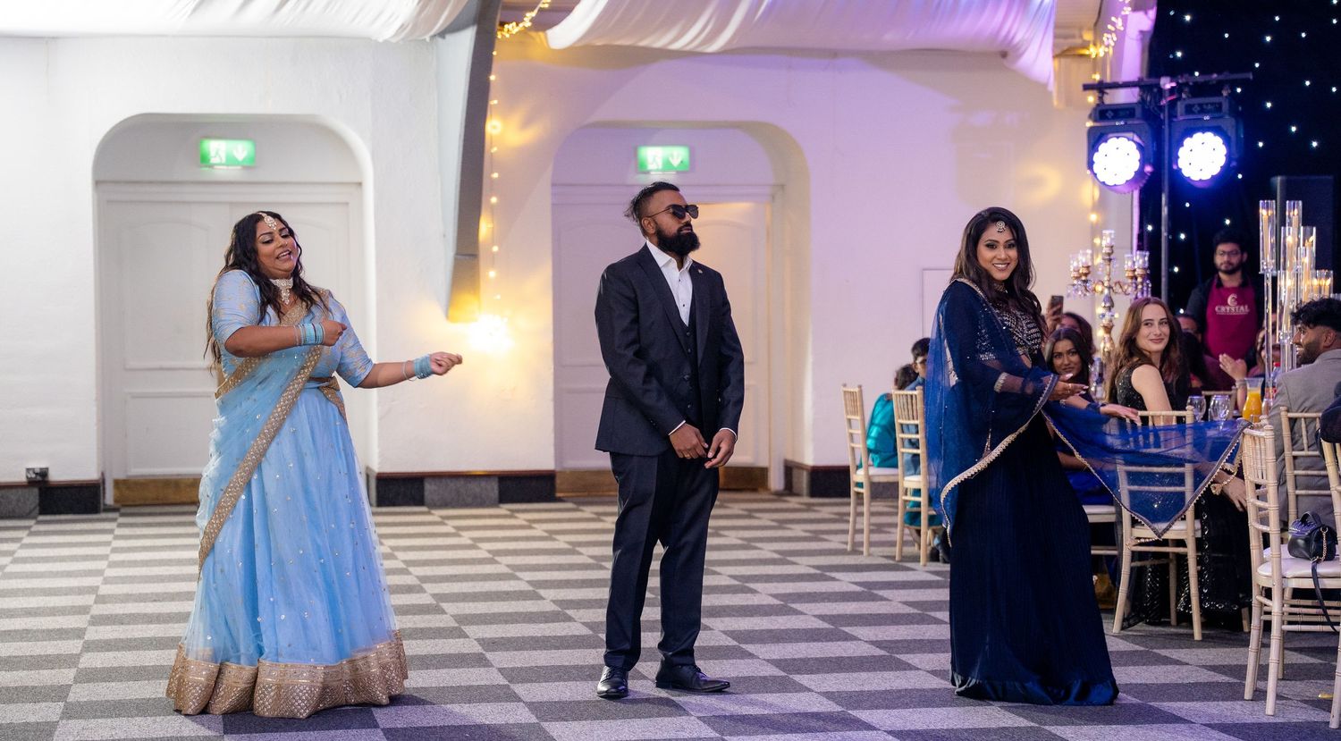 Guests performing a dance in traditional Indian outfits at an elegant wedding reception venue.