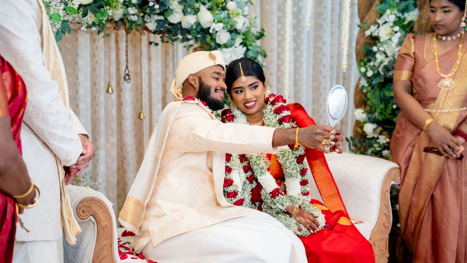 Bride and groom share intimate moment with mirror during traditional South Indian Hindu wedding ritual.