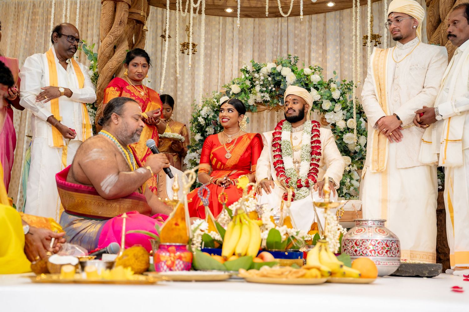 South Indian wedding ceremony with bride, groom, priests, and guests gathered at decorated mandap.