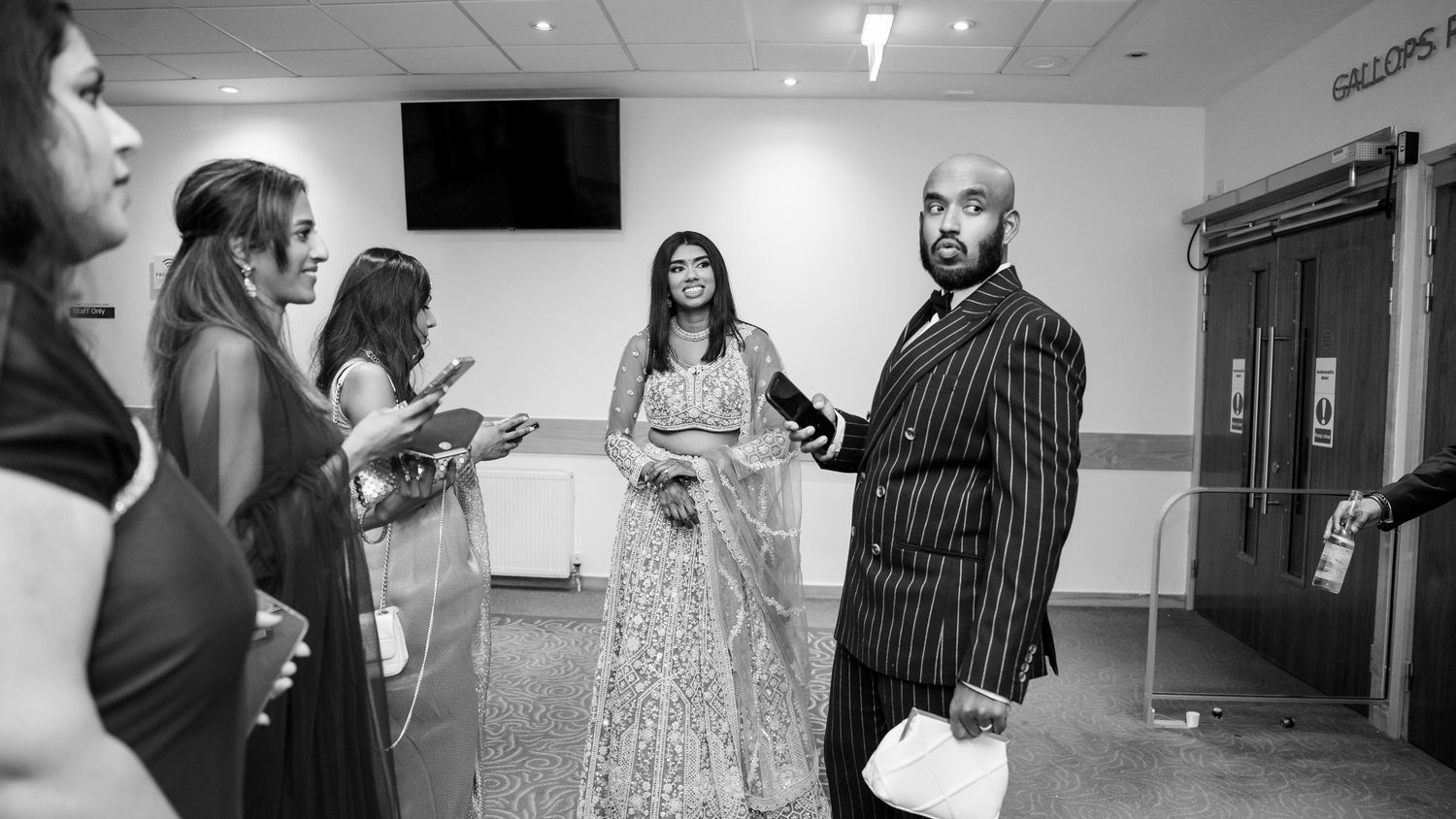 Black and white photo of elegantly dressed guests chatting in a wedding venue corridor.