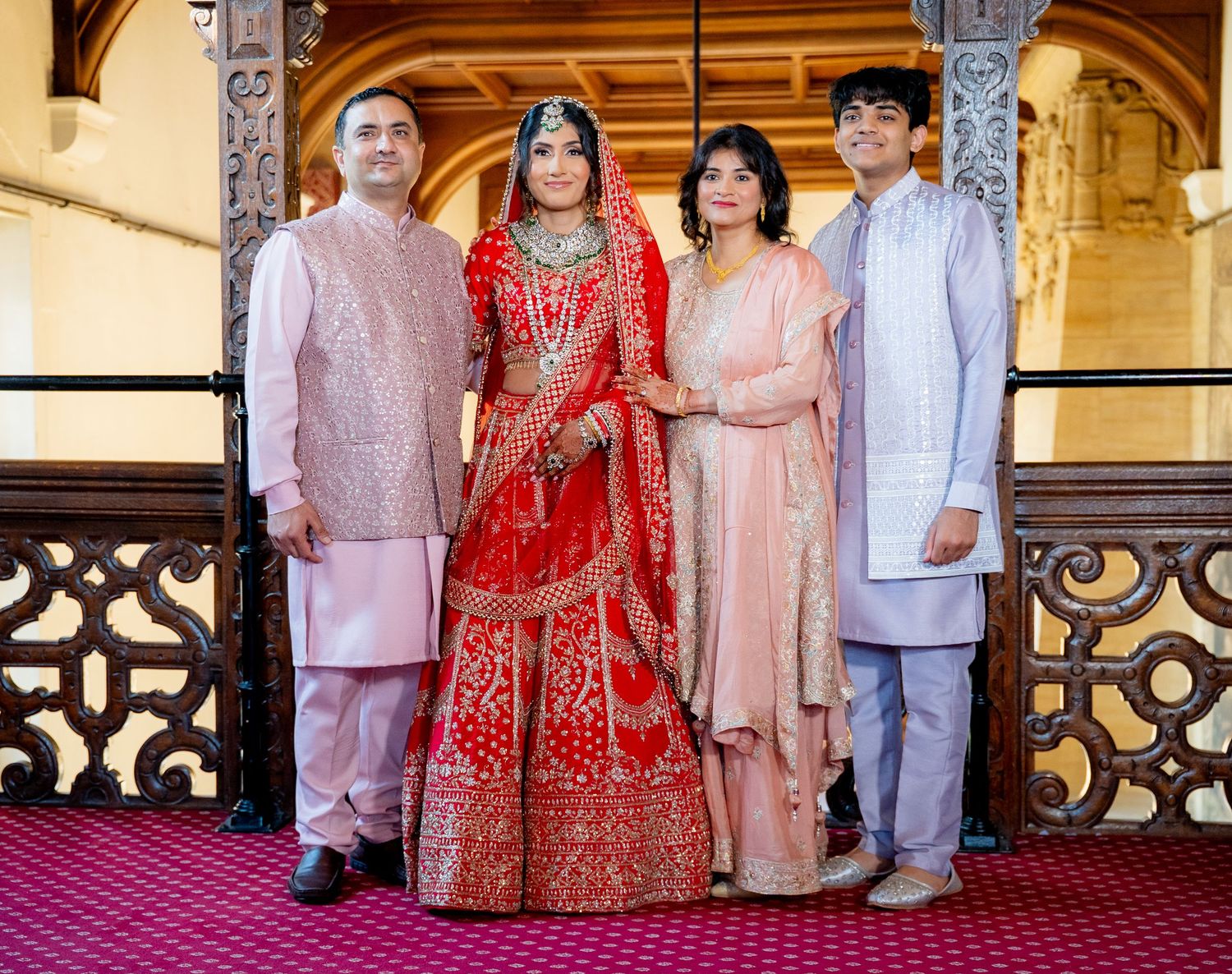 Indian bride in red lehenga posing with family including parents and brother at traditional wedding.