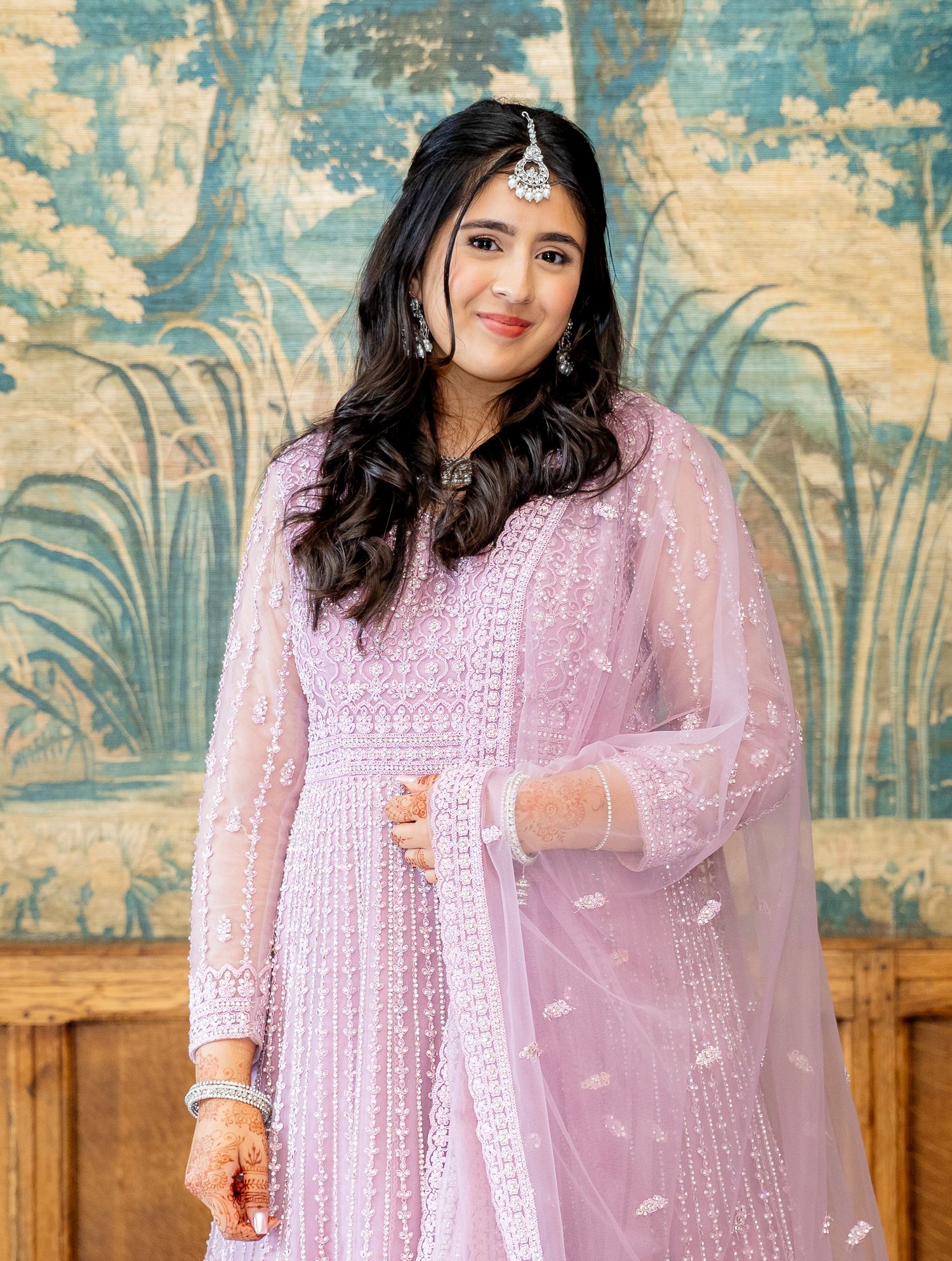 Young woman in elegant light pink embroidered anarkali suit with dupatta and maang tikka at a formal event.