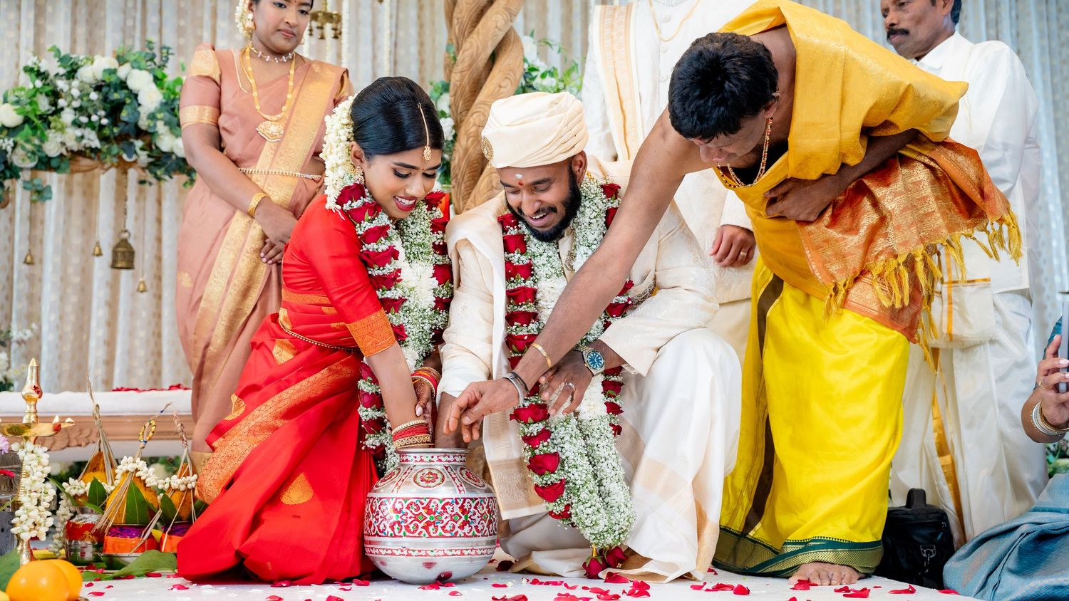A bride and groom perform traditional South Indian wedding rituals with family members in colorful silk attire.