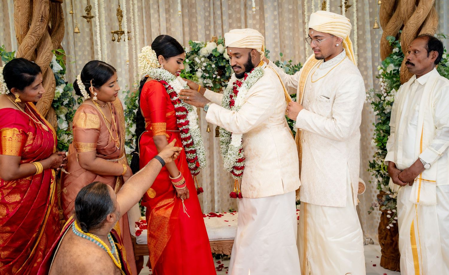 Groom places garland on bride during traditional South Indian Hindu wedding ceremony on ornate stage.