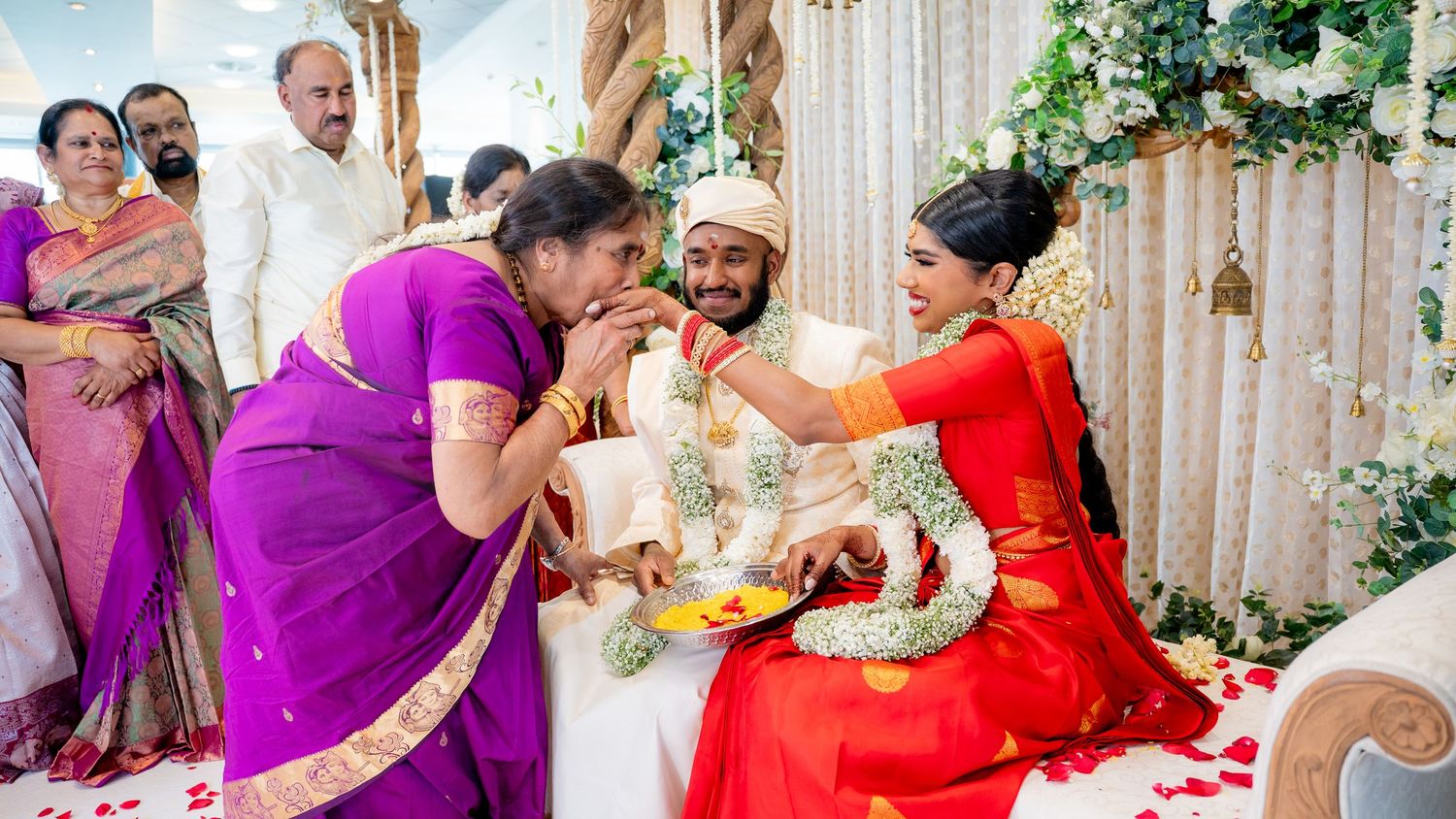 Joyful family blessing Hindu bride and groom with garlands at traditional Indian wedding celebration.