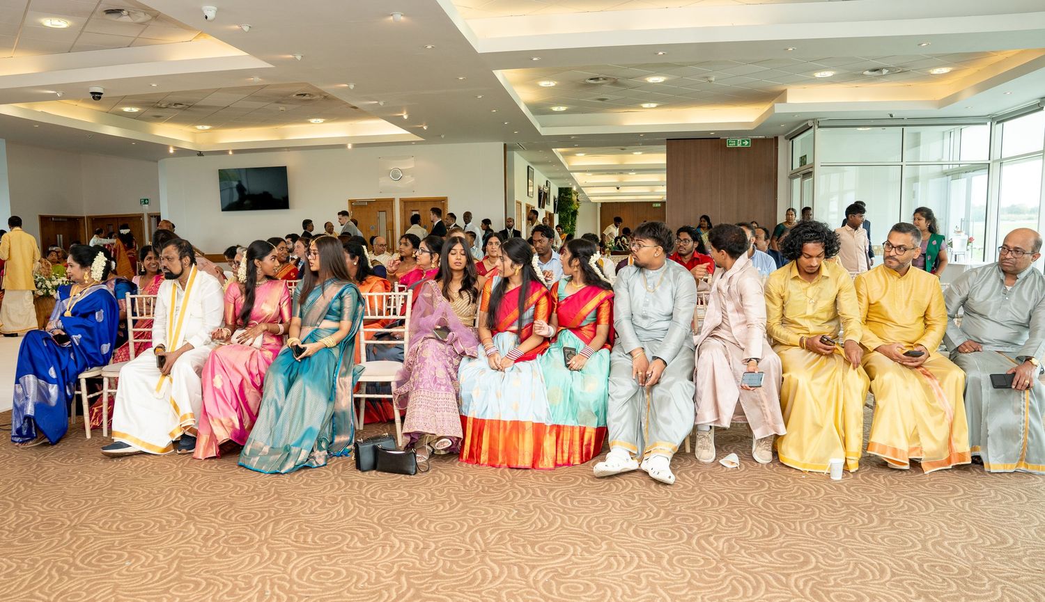 Guests in colorful traditional Indian attire seated at a South Indian wedding celebration ceremony.