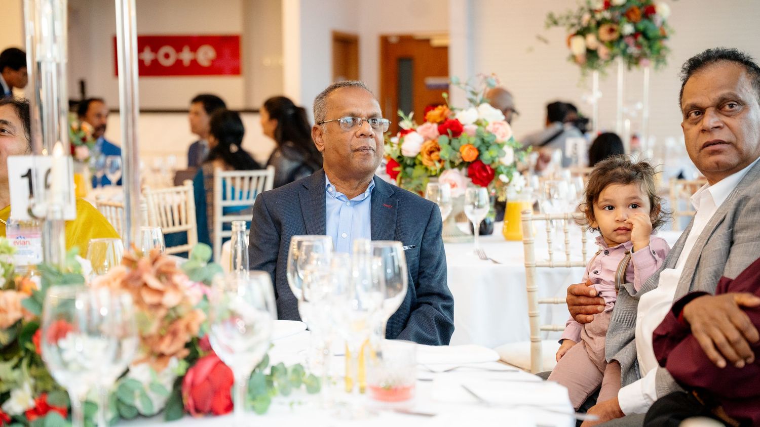 Elderly man holding a baby at a beautifully decorated wedding reception dinner.