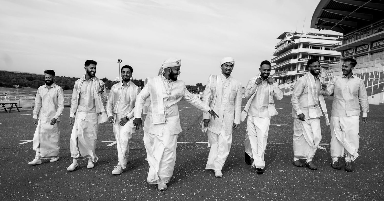 Group of men in traditional white South Asian attire walking confidently at a racetrack in a black and white photo.