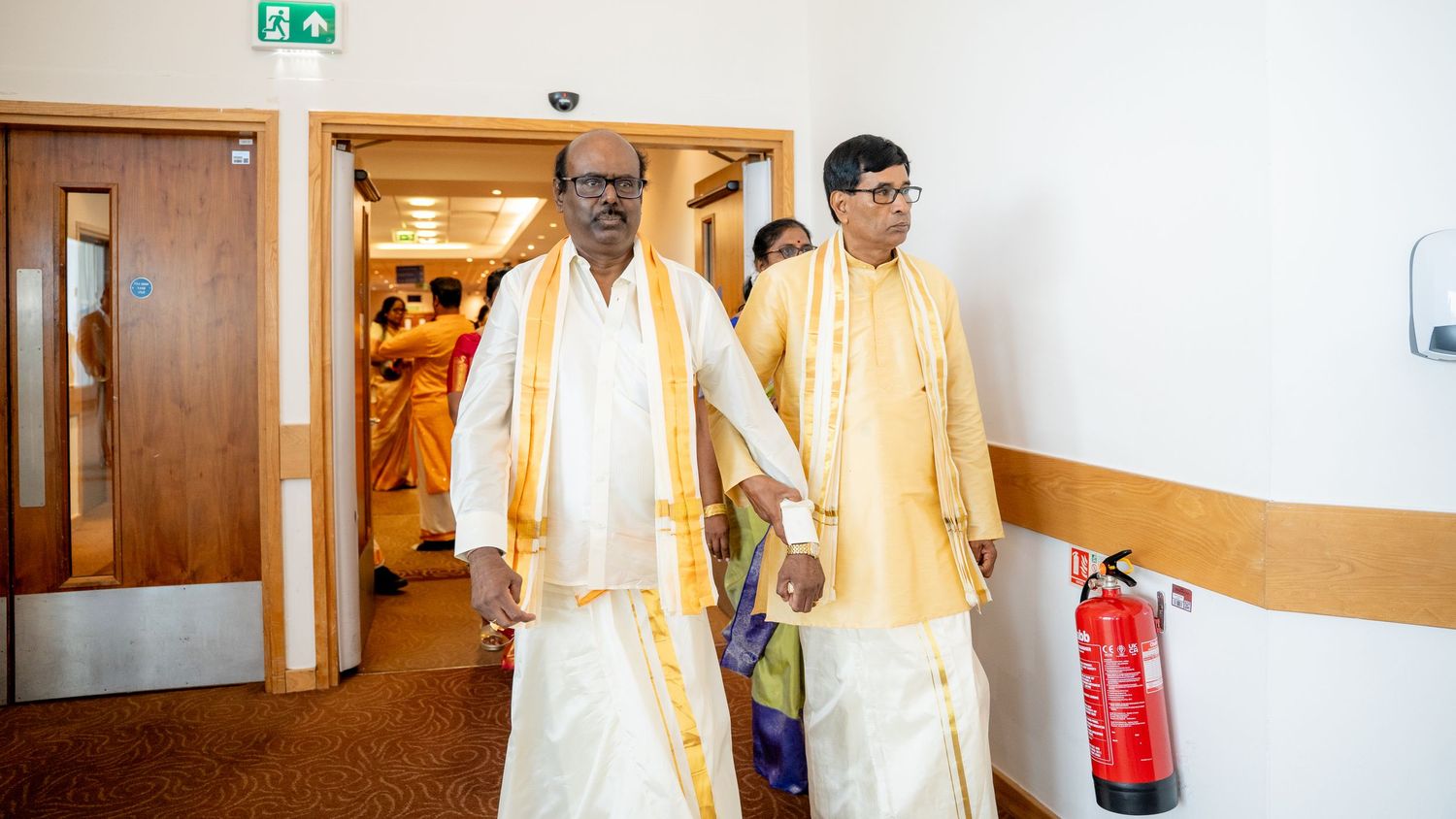 Two men in traditional Indian attire walk through a corridor during a cultural or religious ceremony.
